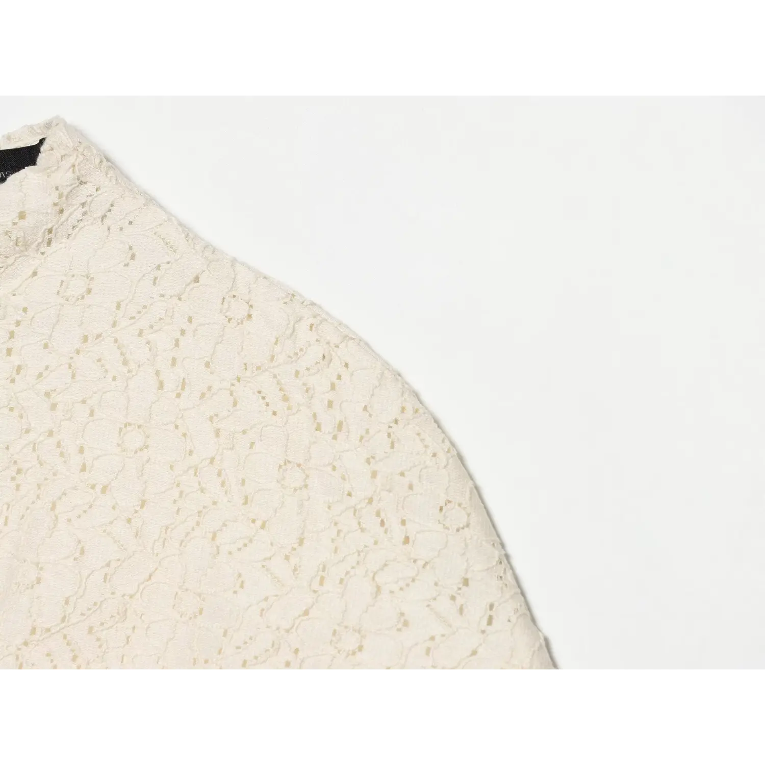 Extreme close‑up of cream floral lace fabric at dress shoulder, showing intricate hollow lace weave texture