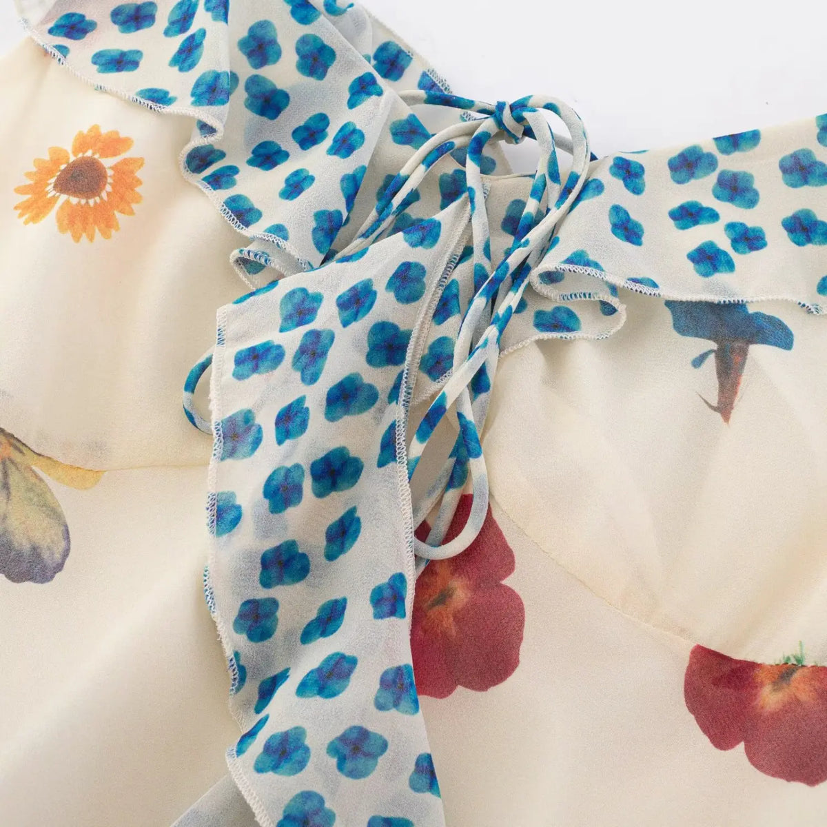 Close‑up of blue polka dot ruffle tie shoulder detail on cream floral maxi dress