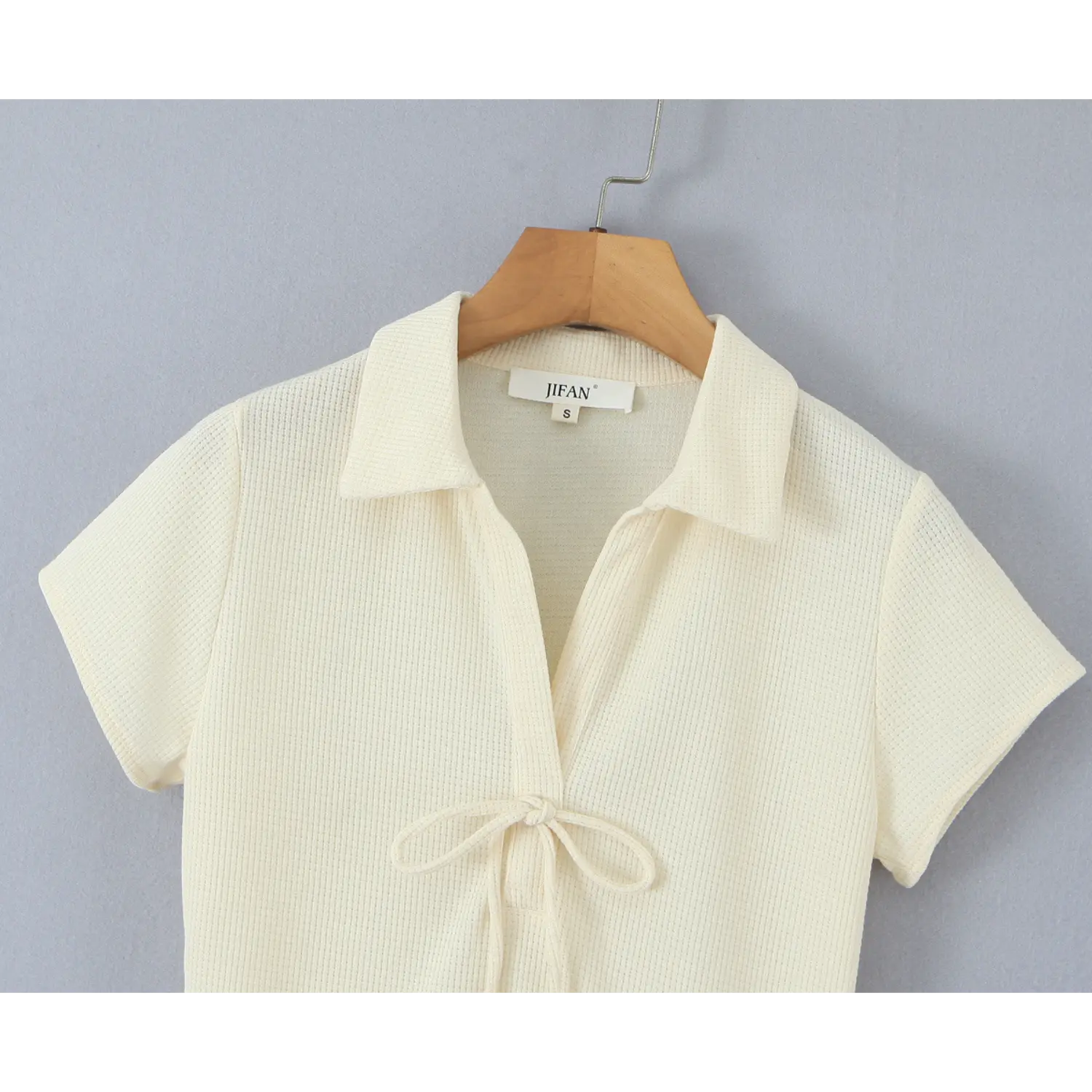 Close‑up of polo collar and front tie knot on cream waffle knit mini dress hanging on wooden hanger