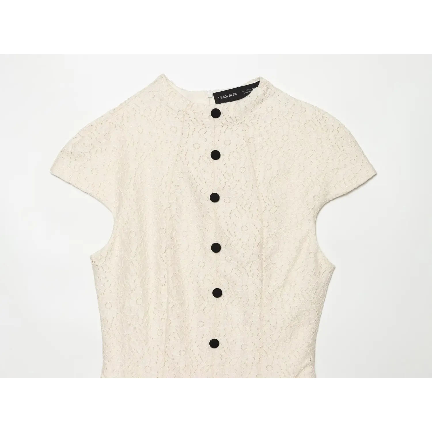 Close‑up shot of cream lace dress bodice, stand collar, cap short sleeve, vertical black button details, floral lace texture