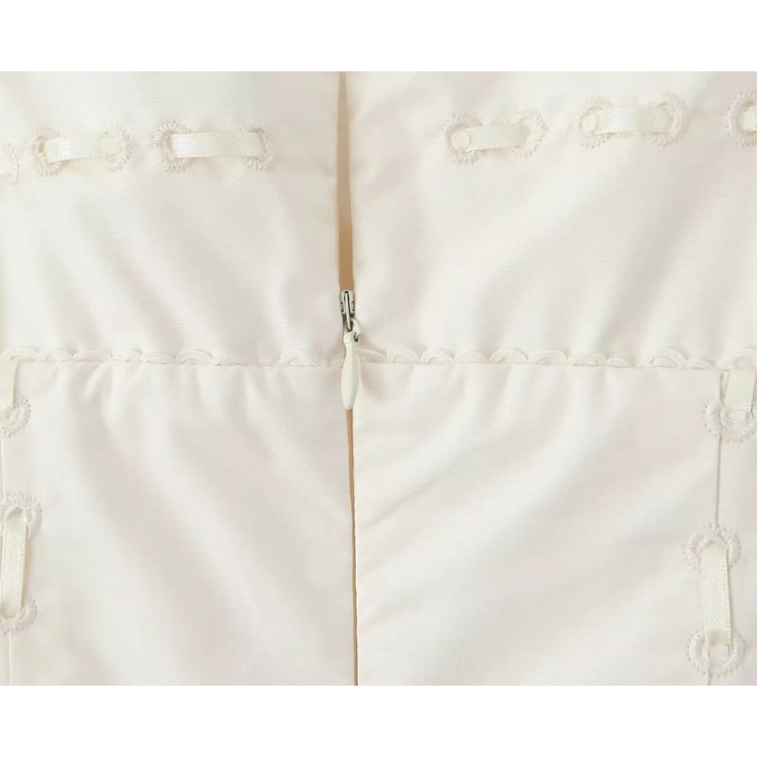 Close‑up view of cream dress back zipper surrounded by vintage loop embroidery and scalloped trim