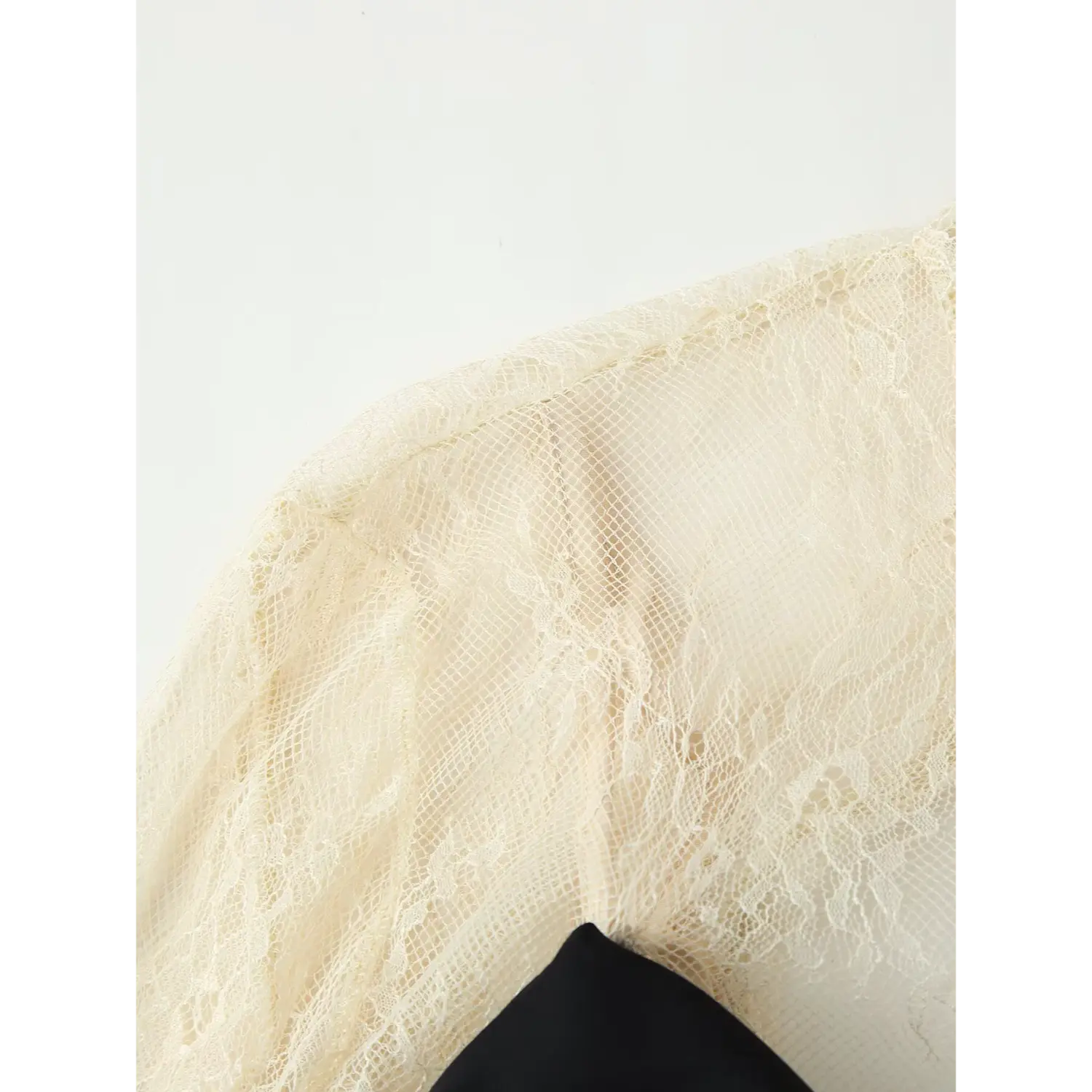 Macro close‑up of sheer cream floral lace shoulder and upper sleeve, fine mesh lace construction