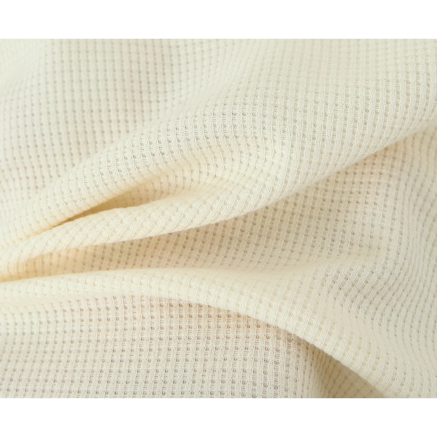 Macro close‑up of cream waffle knit fabric, soft textured knit material