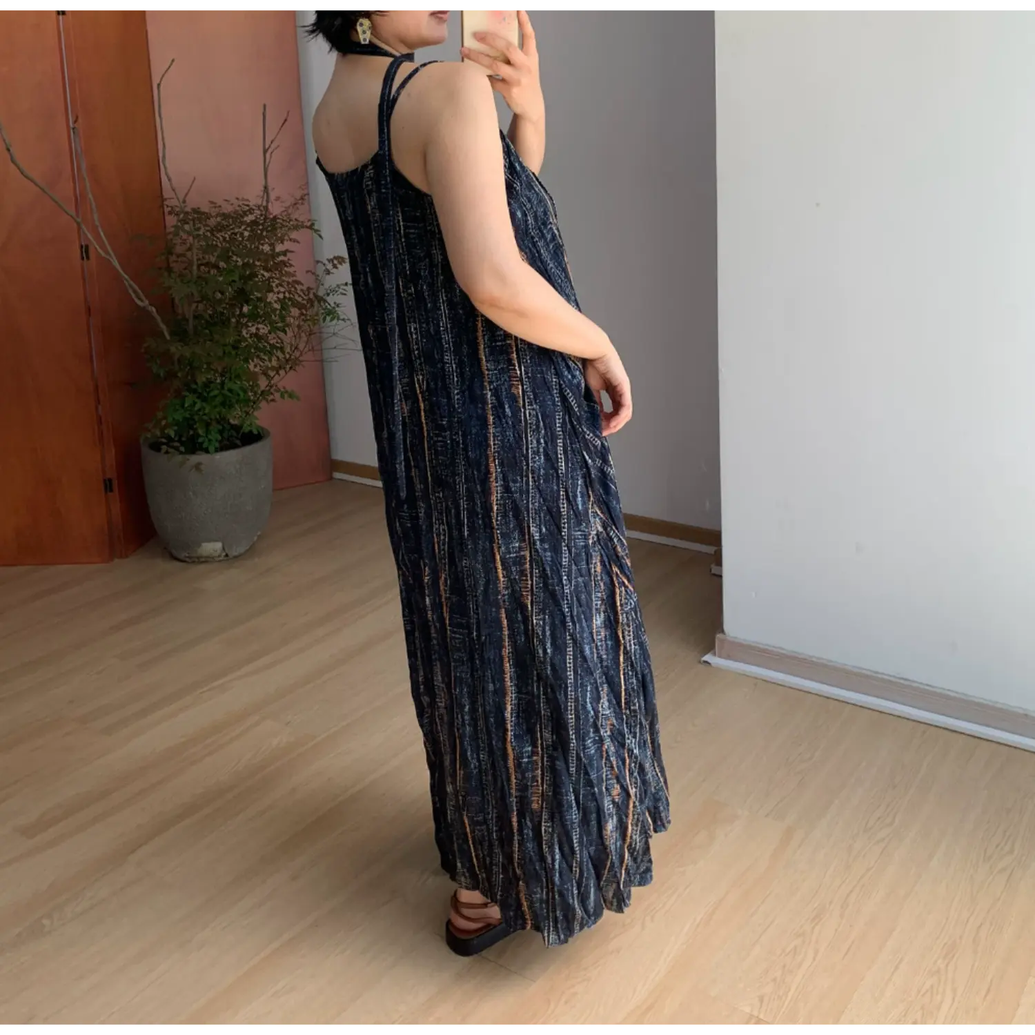 Back side indoor mirror shot of textured sleeveless maxi slip dress, thin adjustable spaghetti cami straps, full loose crinkle swing skirt, vintage vertical faded stripe print on dark navy base, soft wrinkle lightweight fabric drape display