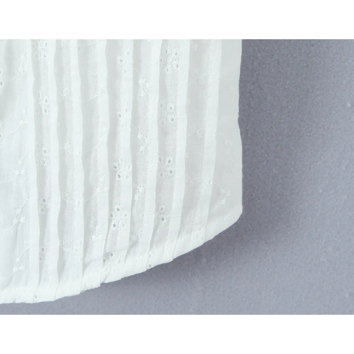 Close-up of the curved hem on a white eyelet embroidered bustier top, showing the finished edge and floral eyelet pattern.