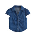 Full front flat lay of dark blue polka dot denim blouse, pointed lapel collar, short cap puff sleeves, front button placket with chest ruched detail, waist shaping seams, curved cropped hem, soft washed denim fabric