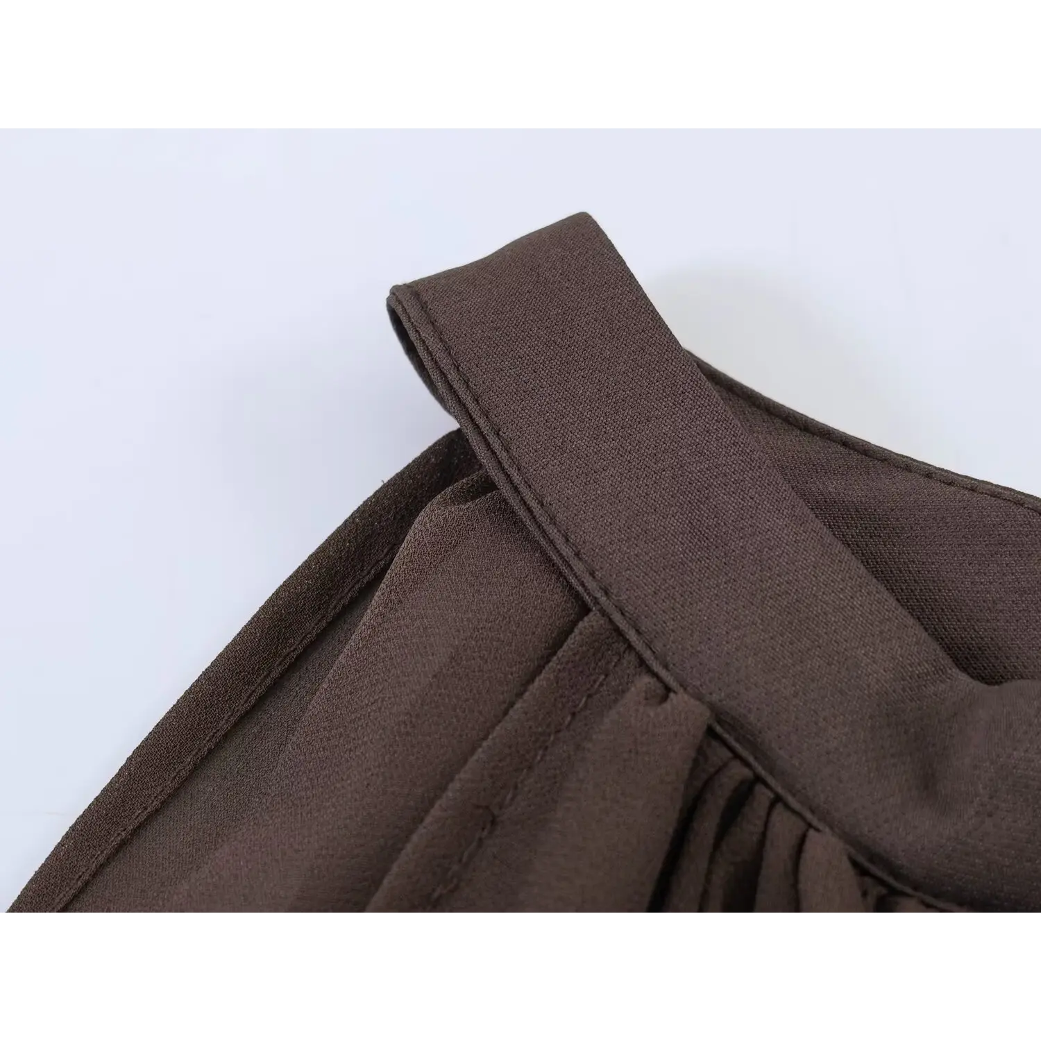 Close-up of solid brown woven halter strap, folded bound edge with straight lockstitch, upper chest shirring junction, matte chiffon overlay fabric