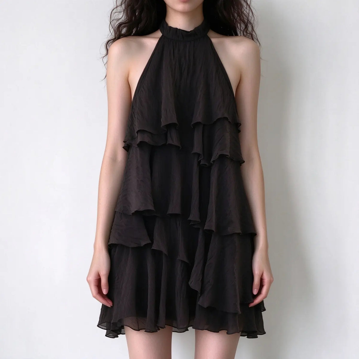 Model wearing dark brown halter neck ruffle mini dress, tiered frill layers, textured lightweight fabric, sleeveless design on plain white background