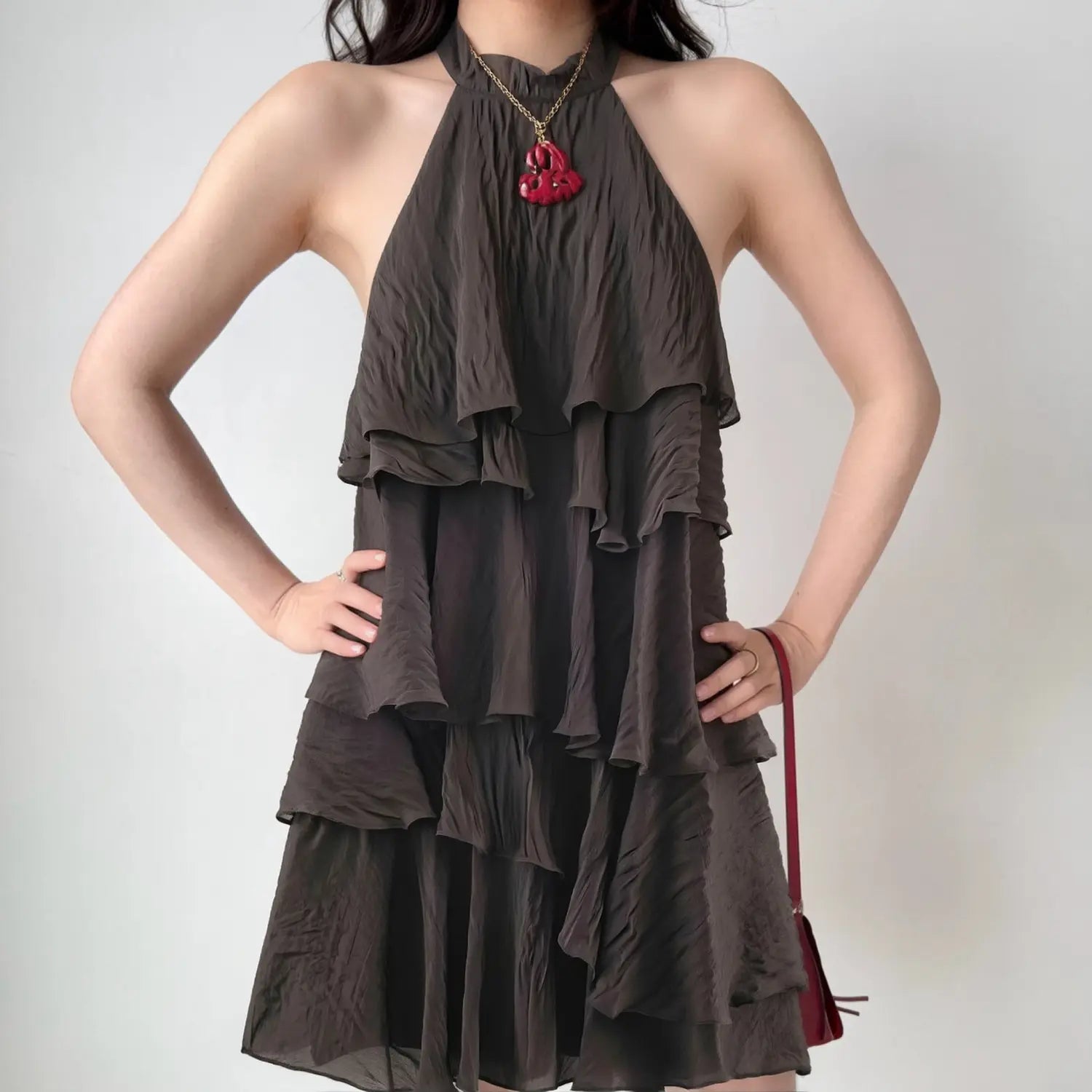 Front lifestyle shot on model of dark brown sleeveless halter neck tiered waterfall ruffle mini dress, crinkled casual summer outfit