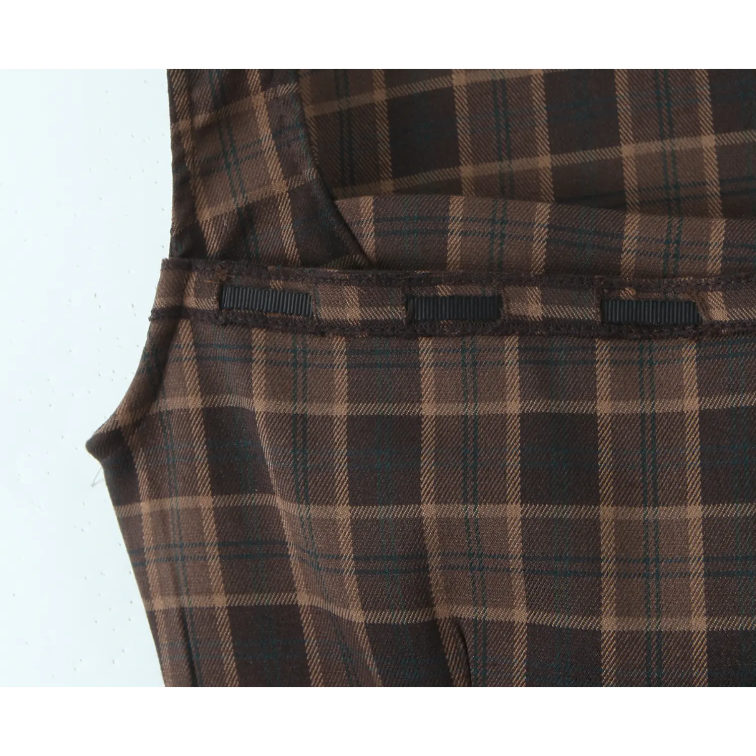 Close-up of horizontal black ribbed ribbon strips sewn across back waist yoke, layered fabric construction, matching plaid outer shell