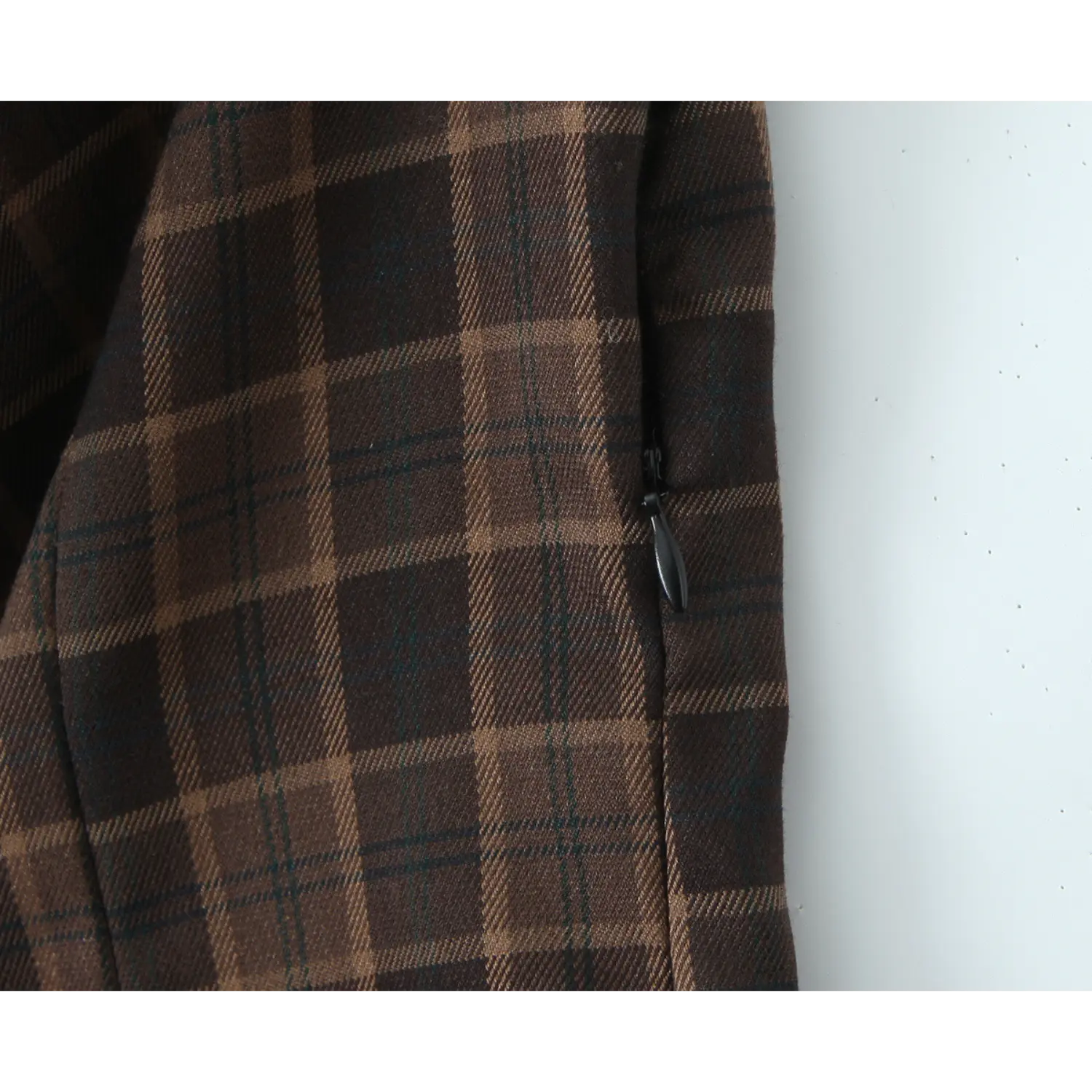 Macro shot of side seam invisible zipper with black fabric pull tab, matching plaid twill woven fabric, precise side seam topstitch
