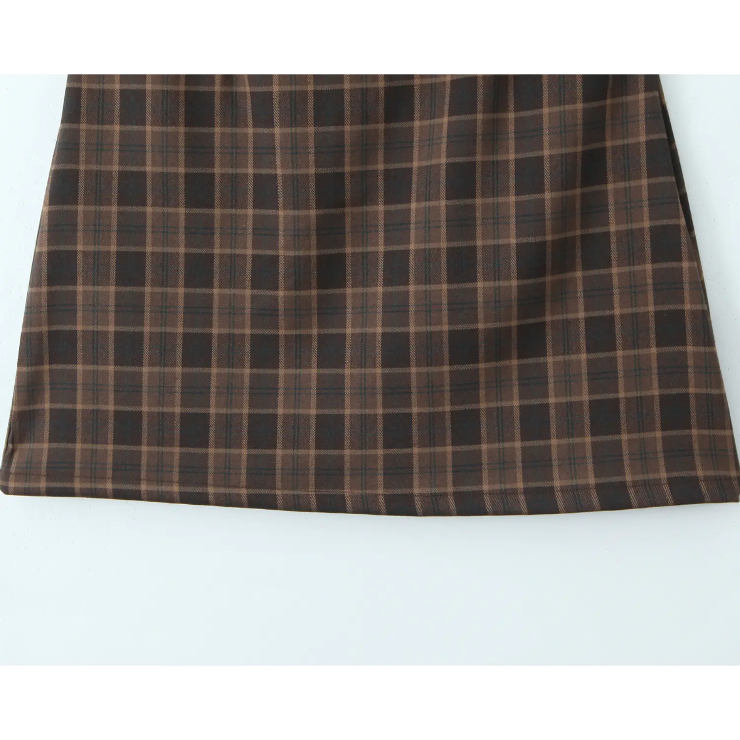 Flat full skirt hem shot, uniform brown multi-line plaid twill fabric, straight finished bottom hem with fine lockstitch stitching