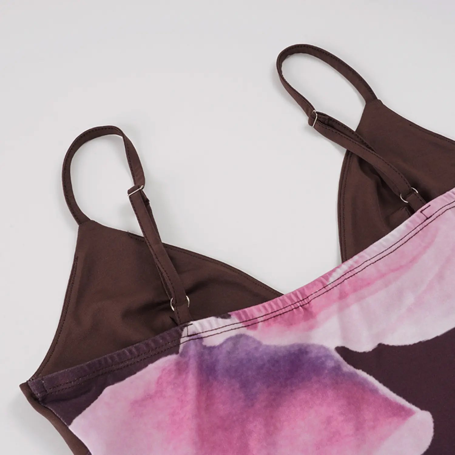 Top-down partial flat studio shot of bodycon slip maxi dress, solid chocolate V-neck bust with double adjustable slider thin straps, large gradient pink watercolor magnolia print on skirt fabric
