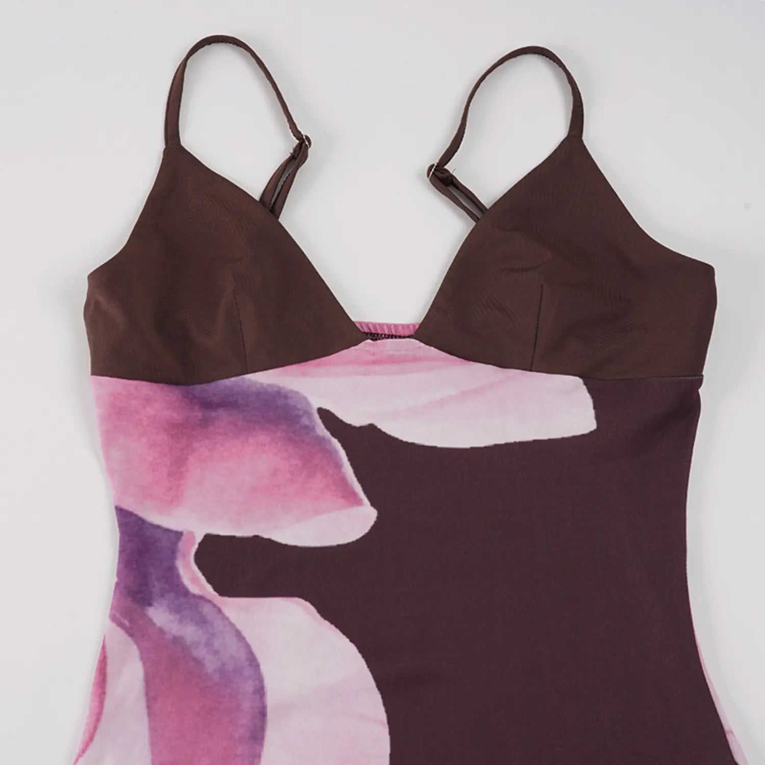 White background flat lay partial shot of bodycon slip maxi dress, solid dark brown V-neck bust panel with adjustable thin straps, large watercolor pink magnolia floral print on skirt section
