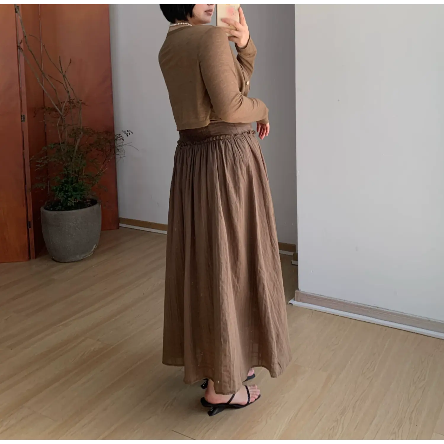 Back side indoor mirror shot of textured empire waist maxi slip dress, full stretch smocked elastic back bodice, single adjustable thin spaghetti strap, ultra flowy gathered A-line long skirt, subtle vertical wrinkle fabric drape display, black square toe slide sandals