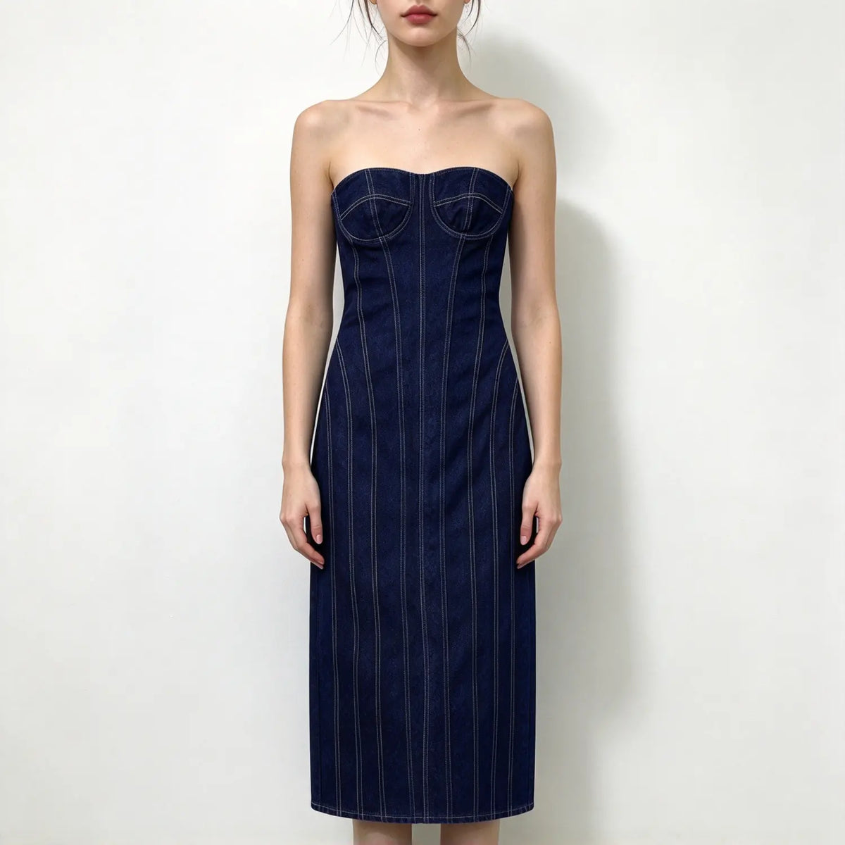 Model wearing dark blue denim strapless corset maxi dress with contrast white stitching, bust cup detail, bodycon fit, plain white background