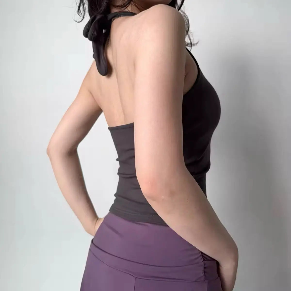 Back view of a woman wearing a dark gray halter tank top, highlighting the halter tie closure and seamless back design.