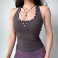 Woman in a dark gray halter tank top, accessorized with a layered cross necklace, showing the shell buttons and keyhole detail.