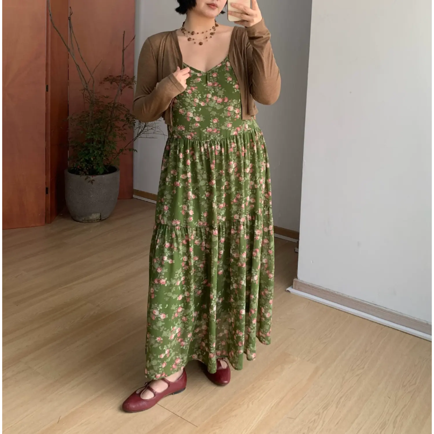Full body indoor mirror shot of forest green tiny pink rose tier slip maxi dress, layered slim light brown long sleeve cropped knit cardigan, burgundy mary jane flat shoes