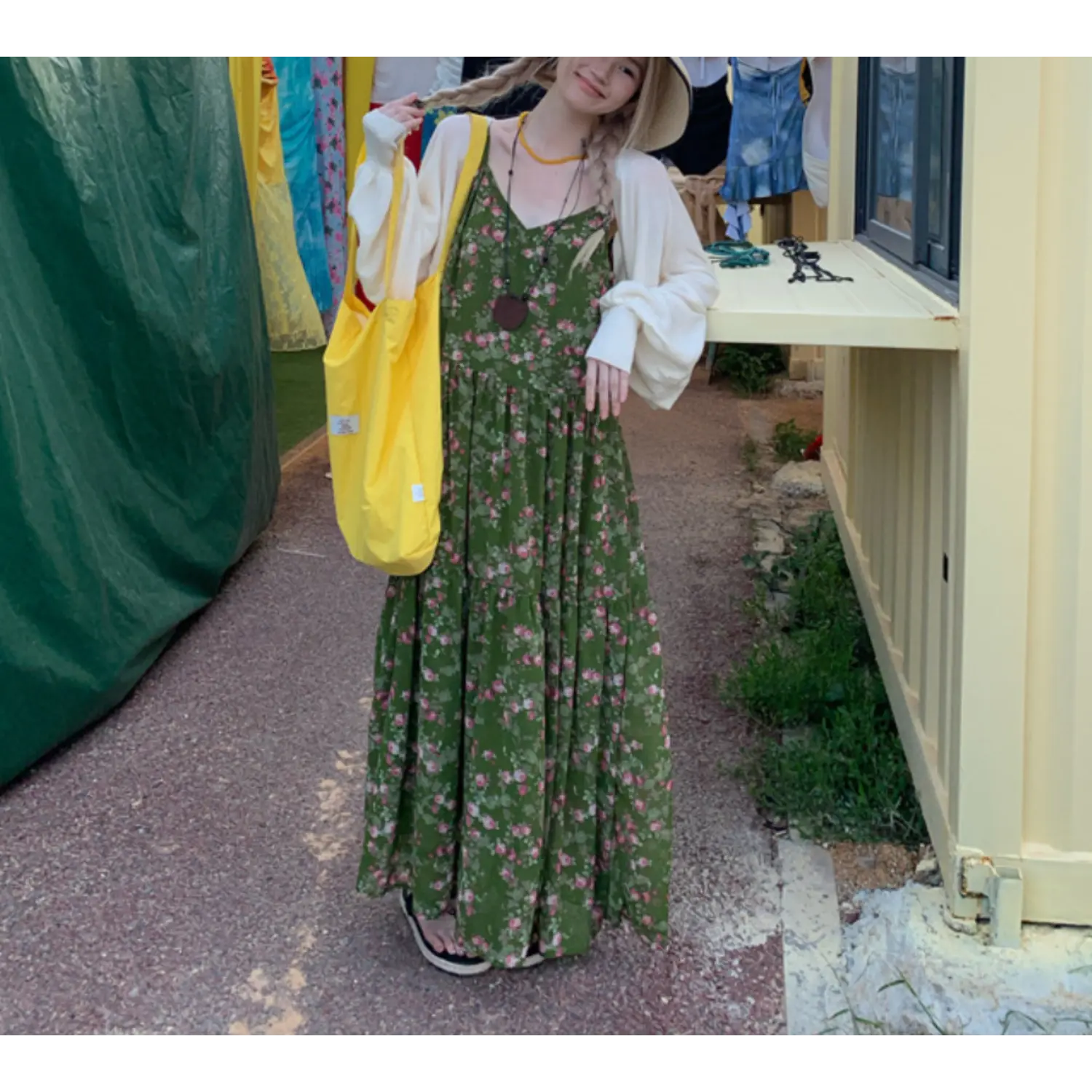 Outdoor alley lifestyle full shot of forest green tiny pink rose tier slip maxi dress, thin V-neck straps, layered oversized cream balloon sleeve knit cardigan, yellow canvas tote bag and slide sandals