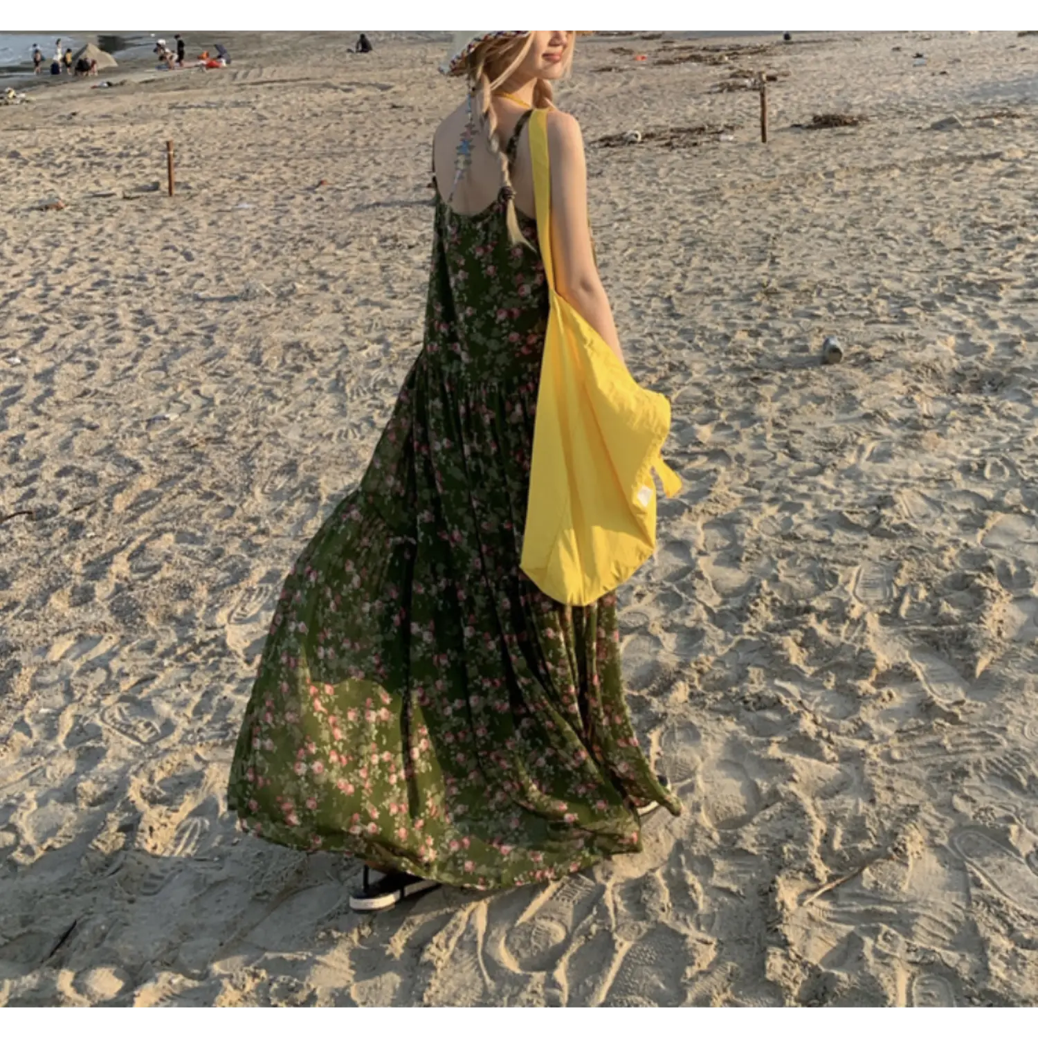 Coastal beach sand outdoor back view shot of forest green tiny pink floral tier slip maxi dress, thin adjustable spaghetti straps, oversized yellow canvas tote slung over shoulder