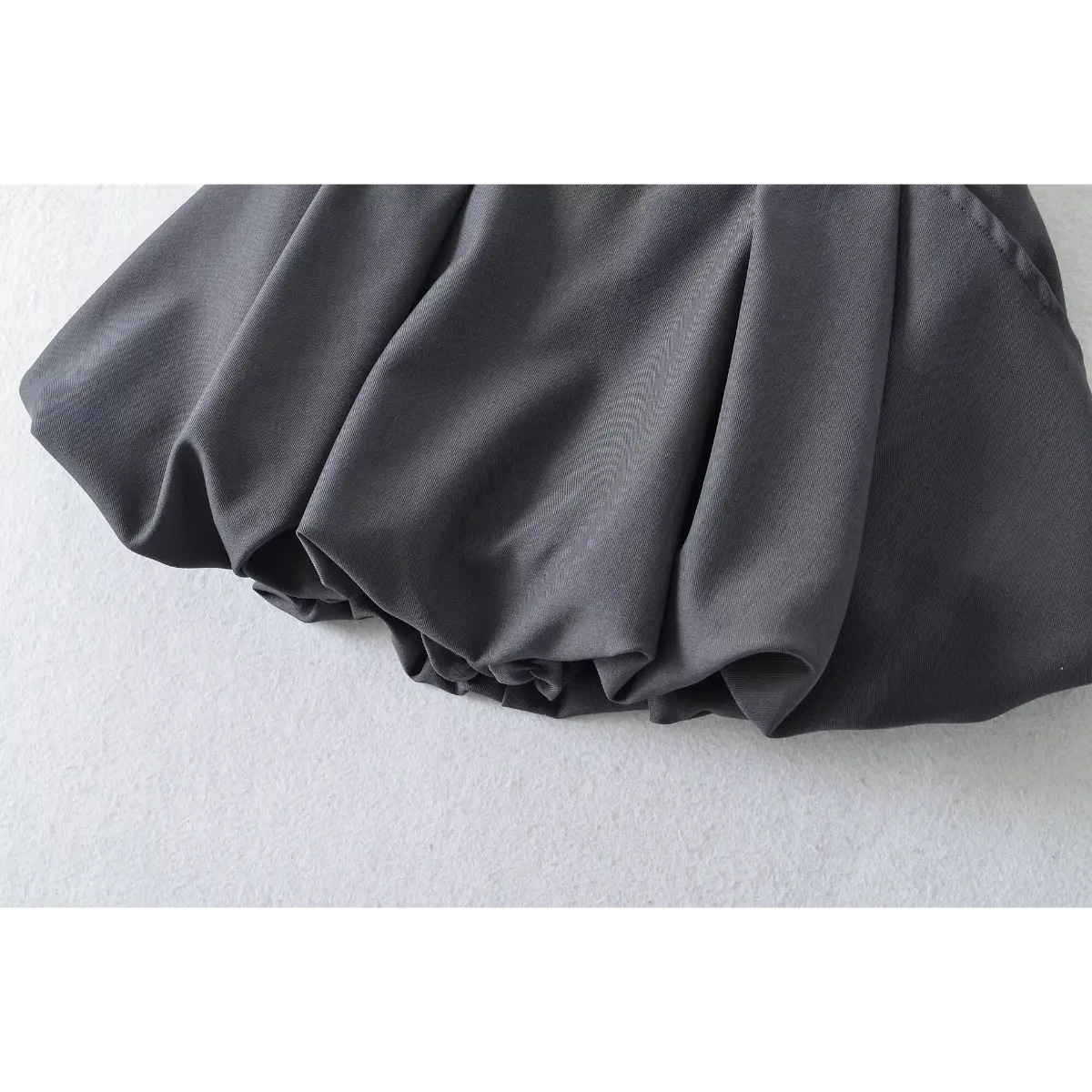 Close-up of the smooth fabric texture and structured bubble silhouette on the dark grey mini skirt