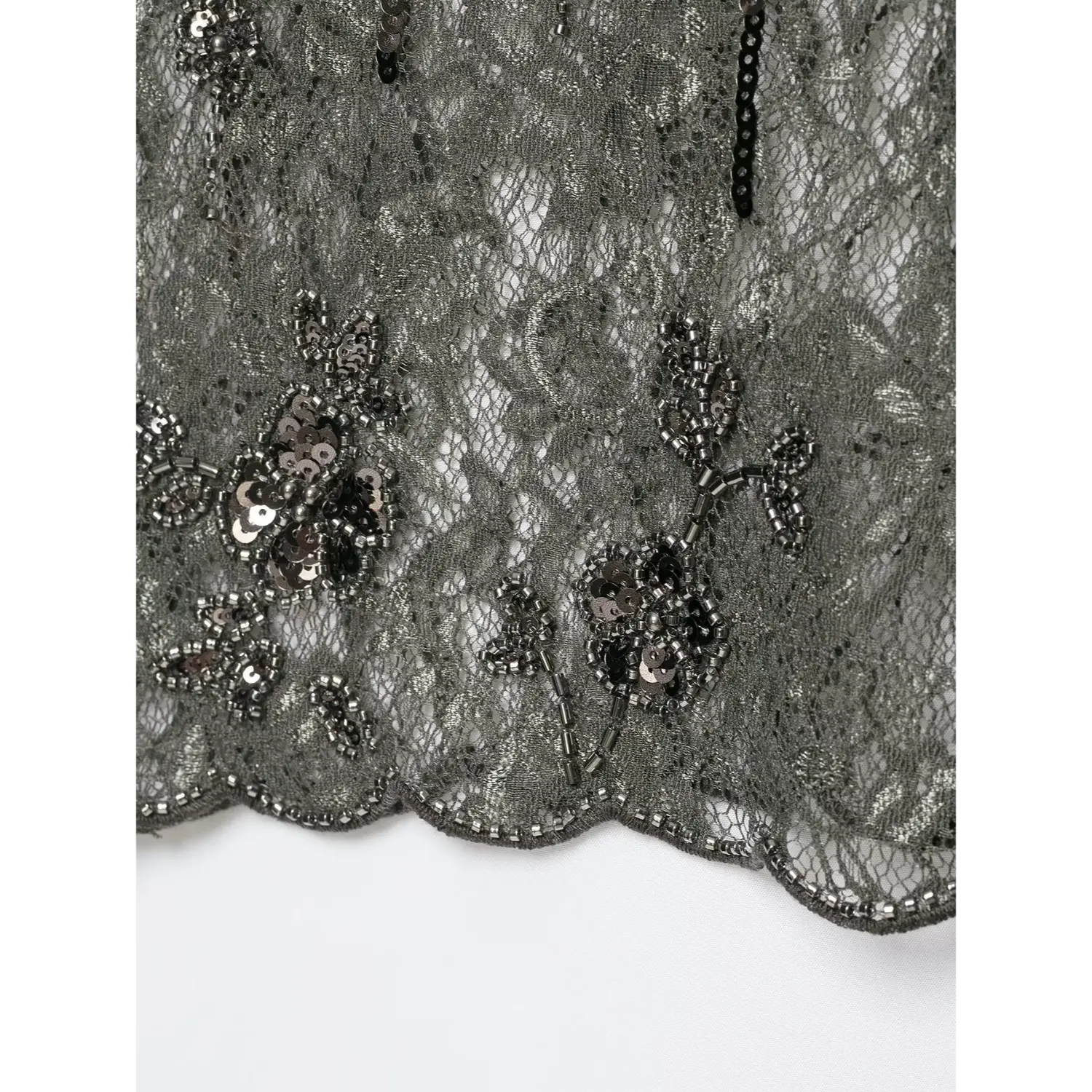 Close‑up scalloped hem detail with hand‑sewn floral bead and sequin embroidery on dark grey sheer lace cami top