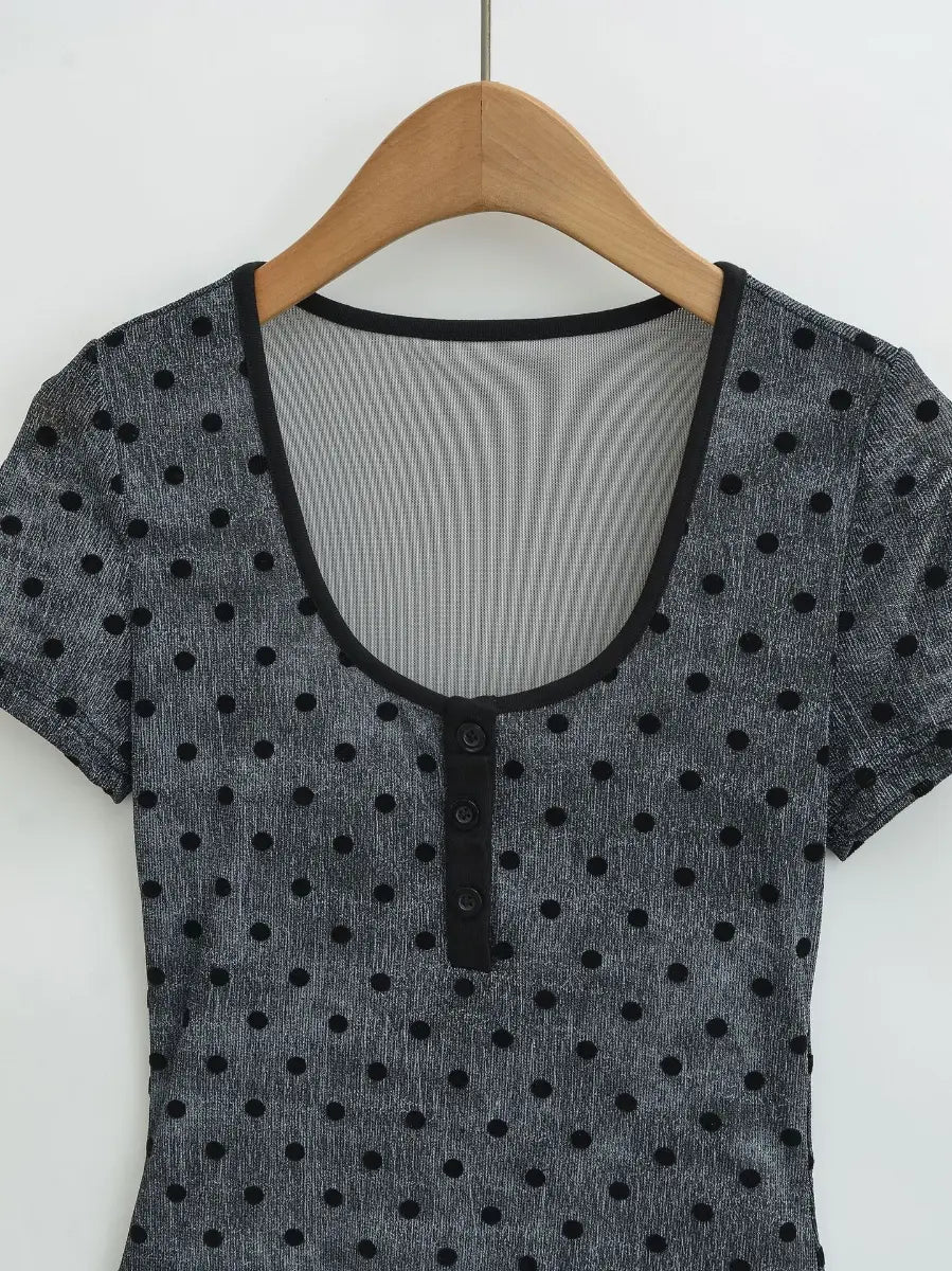 Close-up of the scoop neckline and henley-style button placket on the dark grey polka dot short-sleeve top