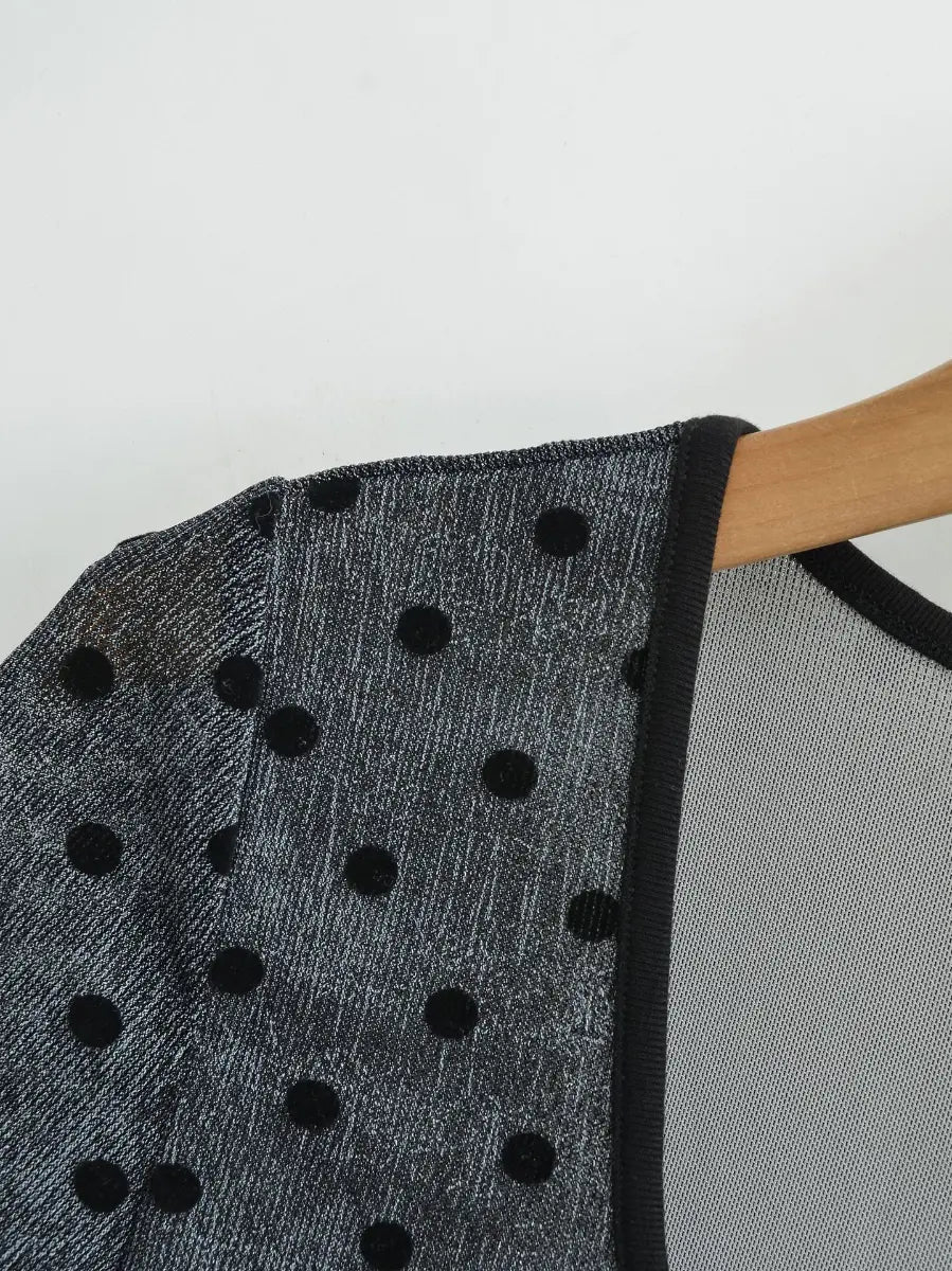 Close-up of the shoulder seam, contrast black neckline trim, and polka dot print on the dark grey top