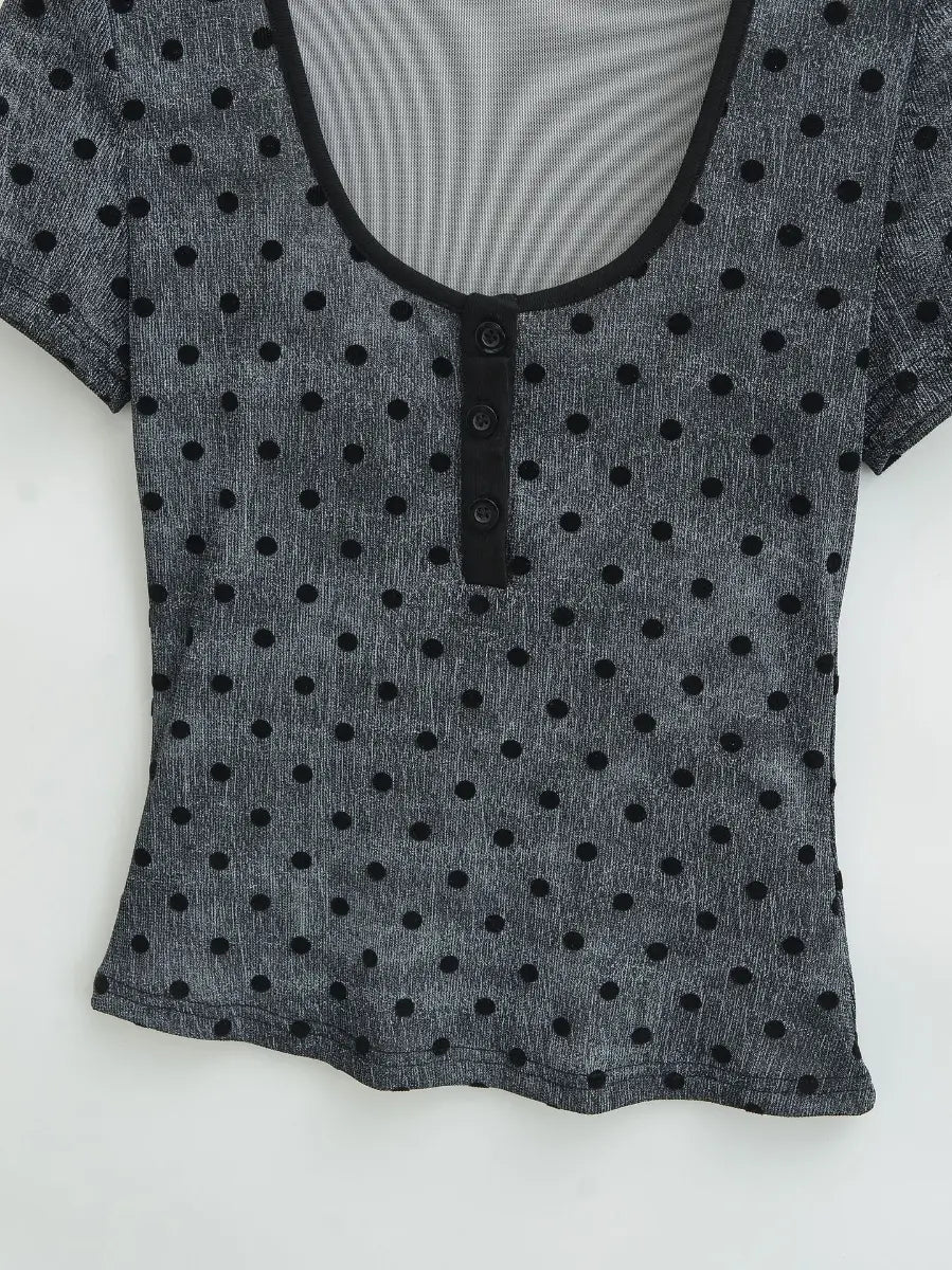 Close-up of the fitted silhouette, finished hem, and henley placket on the dark grey polka dot top