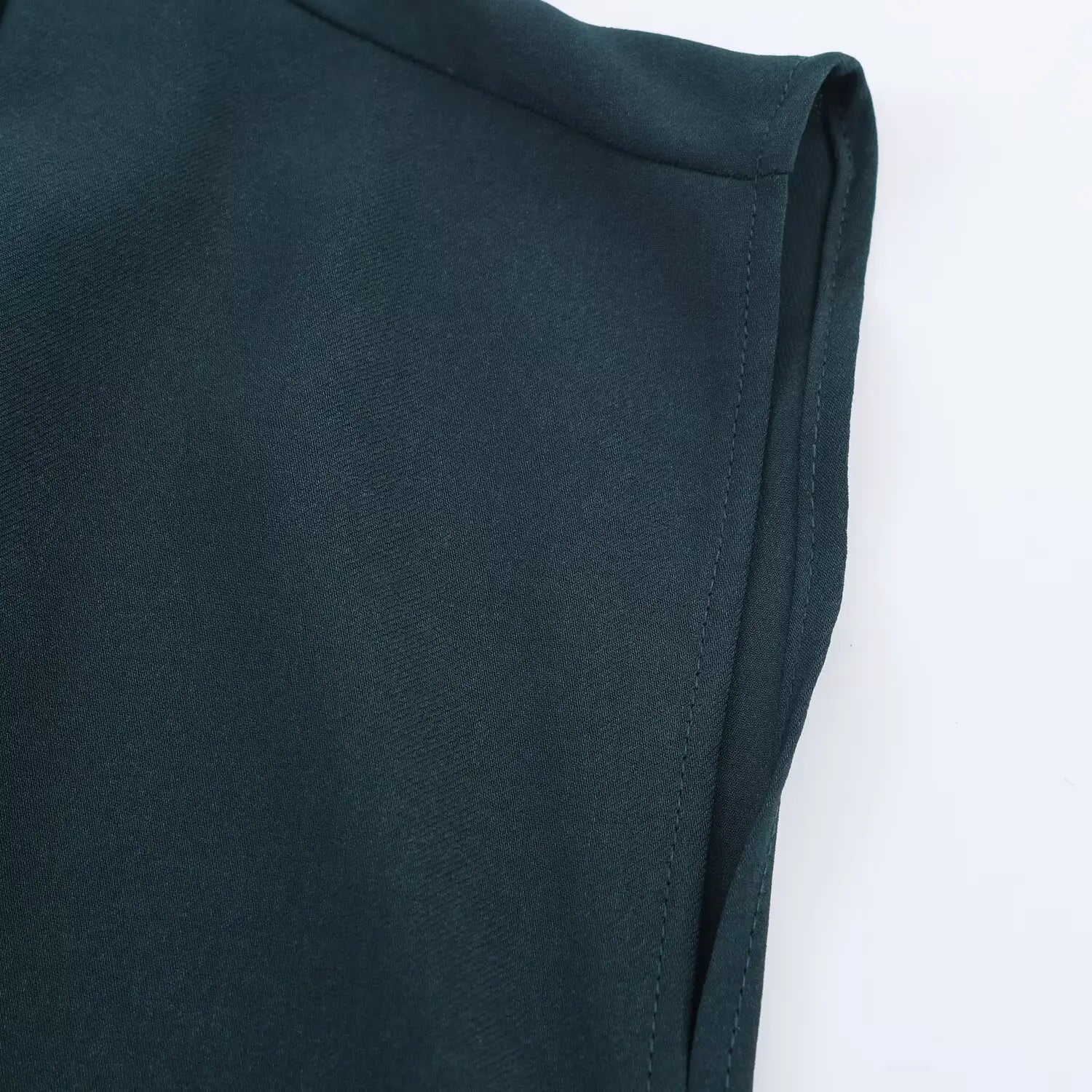 Macro close‑up of cap sleeve finished edge, clean double‑stitched seam on dark teal woven fabric