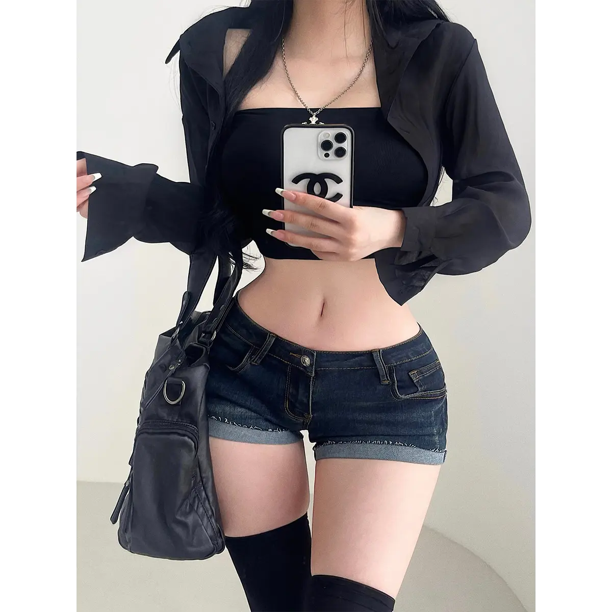 Close-up of a woman wearing dark wash low-rise denim shorts, showing the fit and waistband detail with a black crop top and sheer shirt.