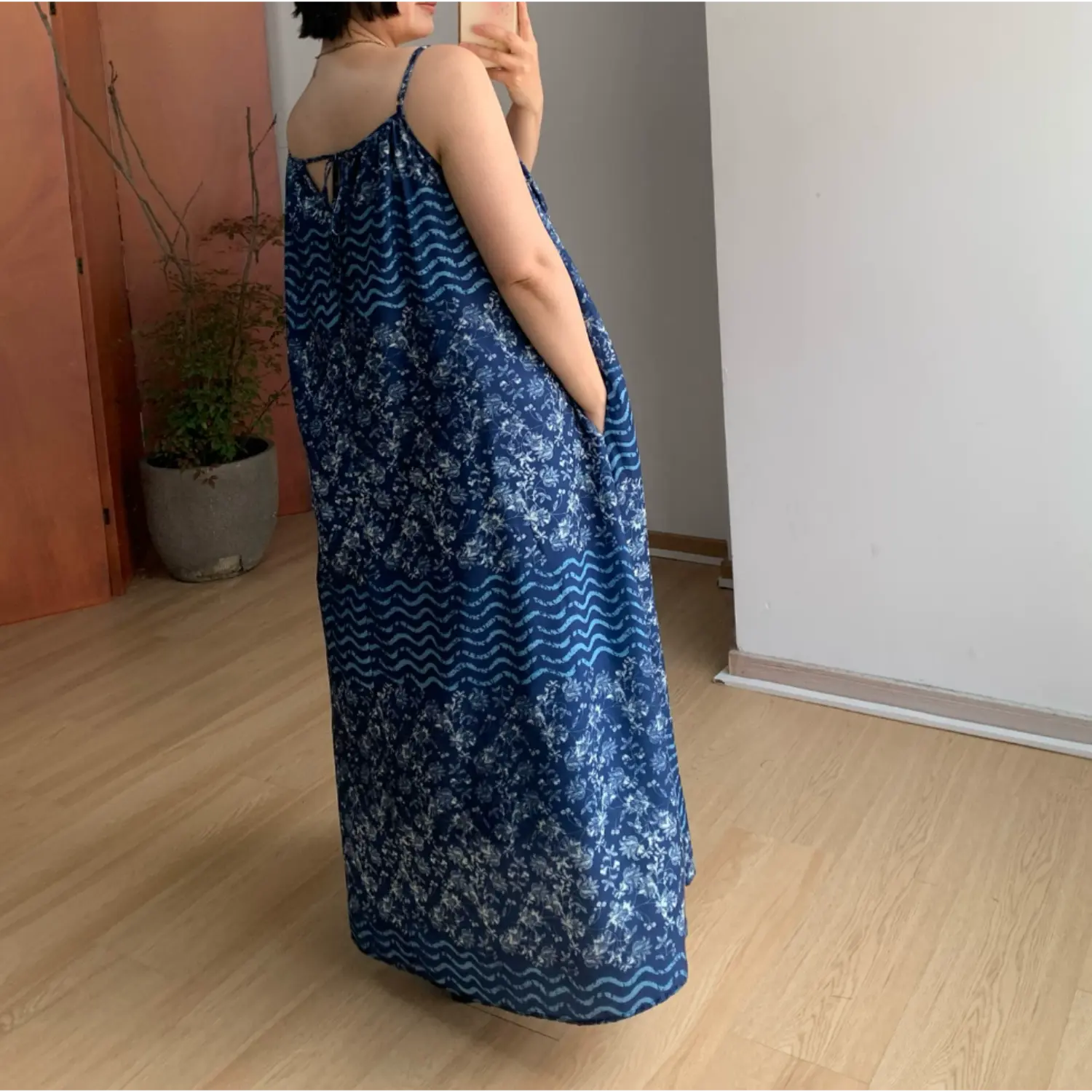 Back side indoor mirror shot of oversized batik cami maxi dress, thin adjustable spaghetti straps, rear keyhole self-fabric tie closure, full loose swing floor skirt, segmented floral & light blue wave batik print panels, soft lightweight drape fabric display