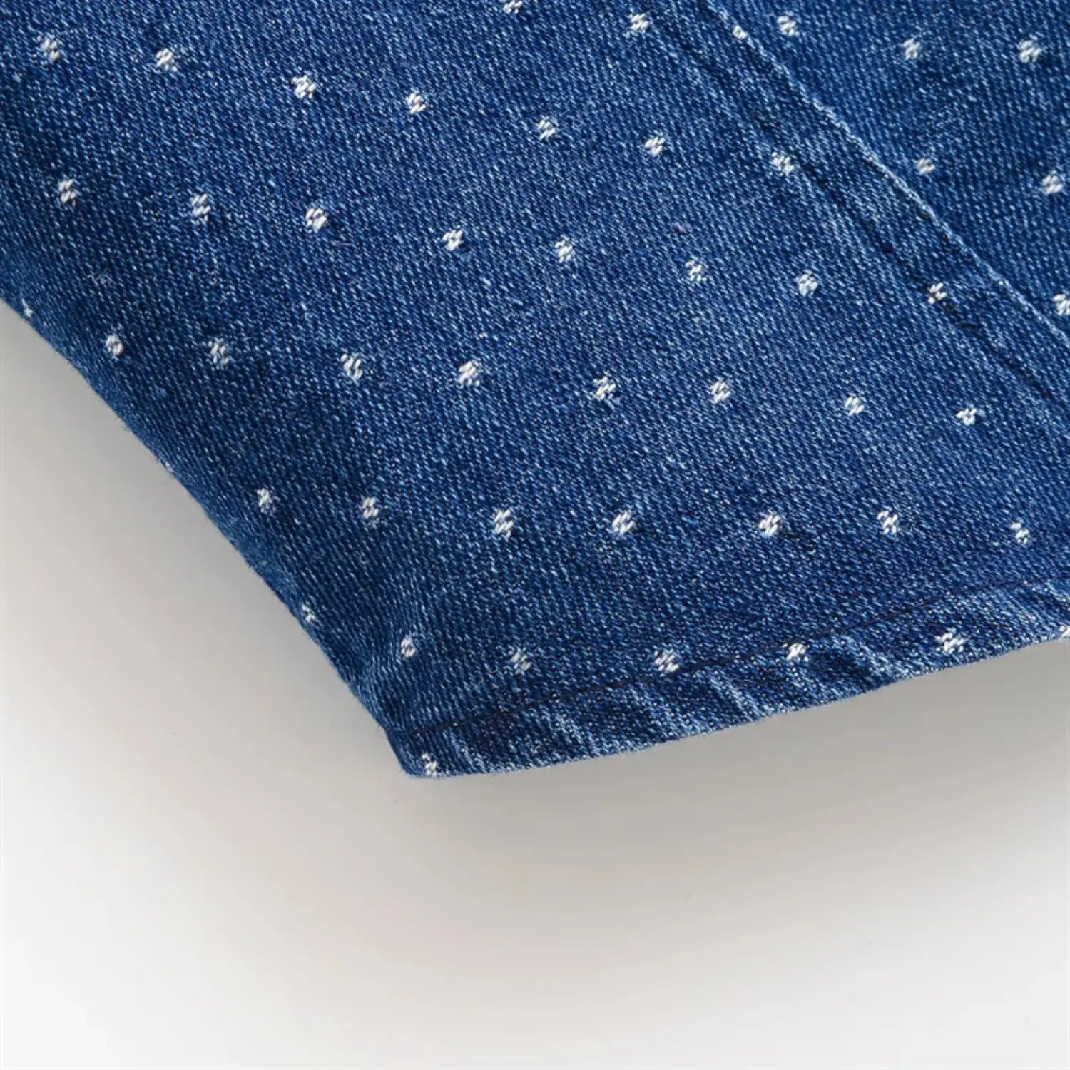 Macro close-up of cap sleeve cuff fabric, dark blue washed denim with tiny white polka dots, twill weave texture, neat hem stitching detail