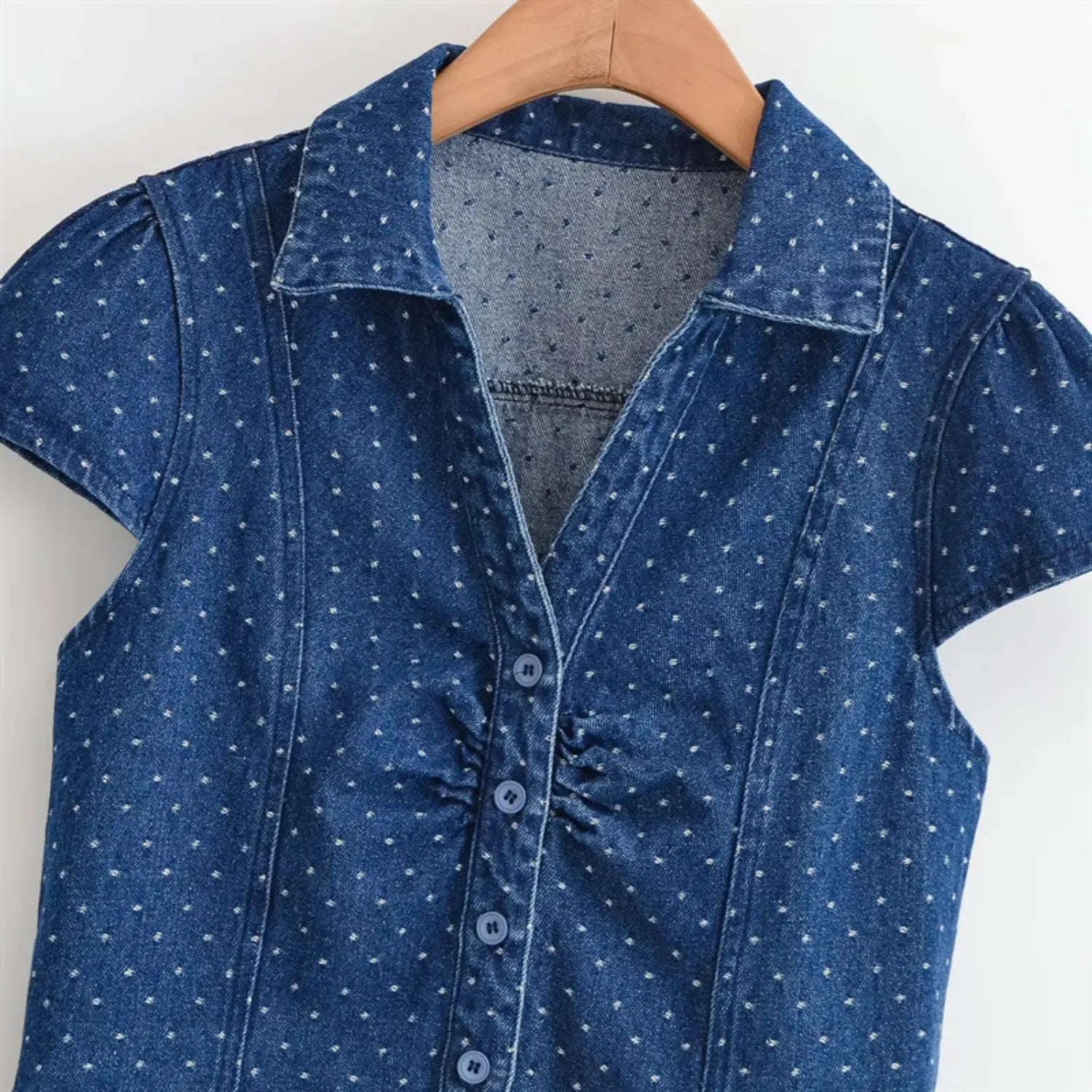 Hanging upper torso close-up, pointed turn-down collar, V-shaped front opening, center ruched gathers, round matching denim buttons, soft washed denim texture