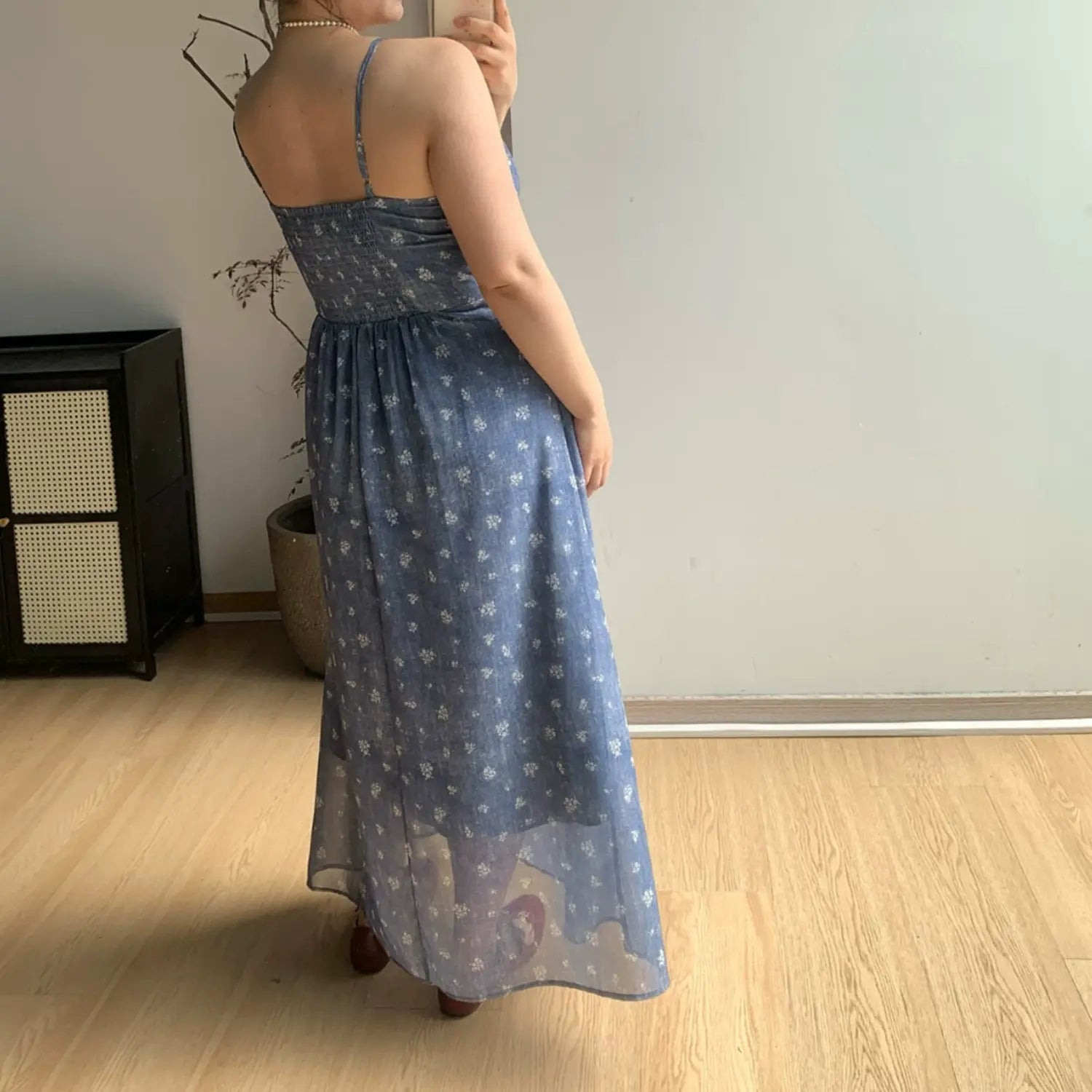 Full back indoor mirror shot of faded blue tiny white floral maxi slip dress, full elastic smocked rear waist panel, thin adjustable spaghetti straps and sheer layered skirt