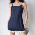 Model wearing dark denim spaghetti strap mini dress, shoulder bow details, double‑layer ruffle hem with white frill, simple plain indoor background