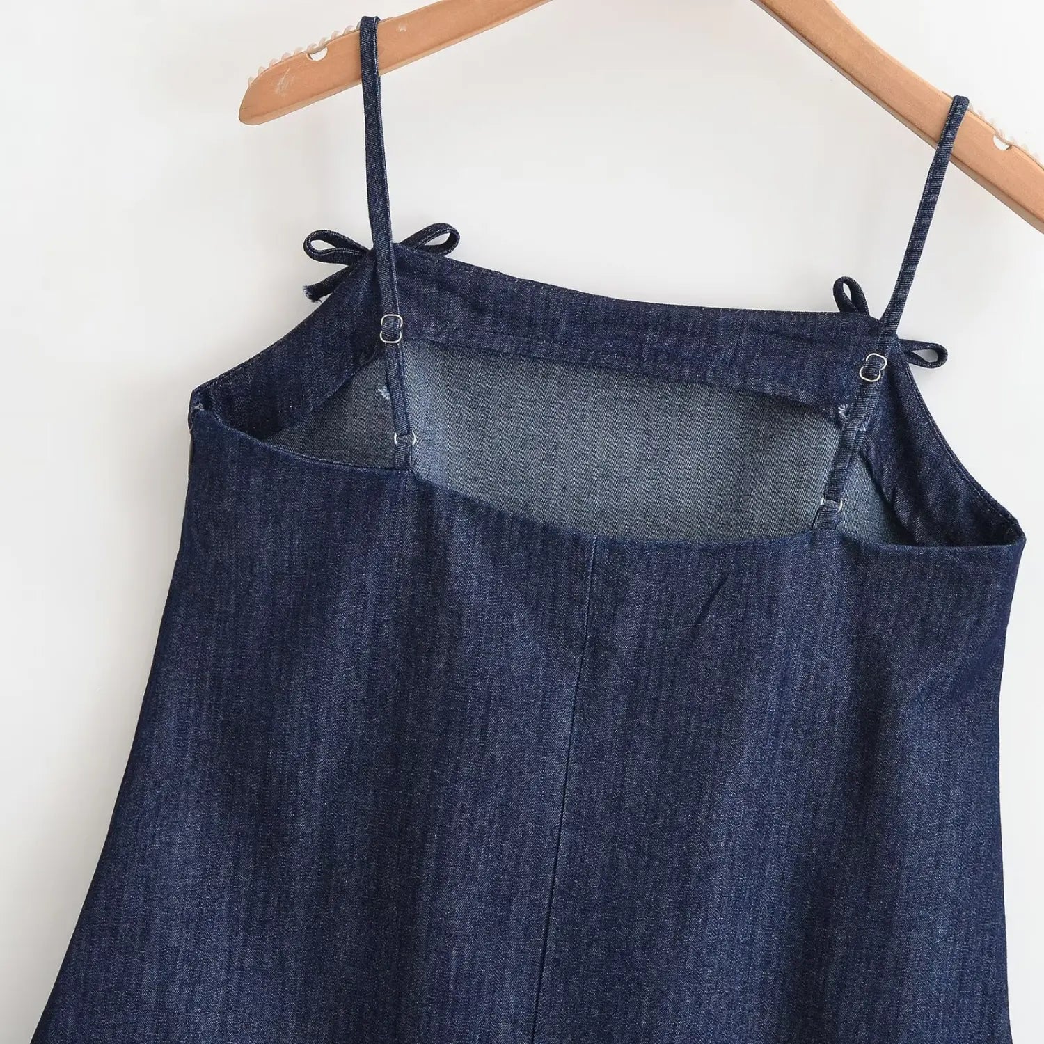 Hanging back view of denim cami dress, adjustable slider straps, square back cut‑out construction, denim woven fabric texture