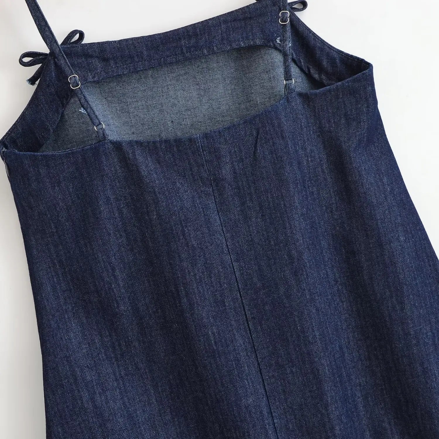 Partial back view of dark denim spaghetti strap dress, square back cut‑out, adjustable metal slider straps, shoulder bow tie details