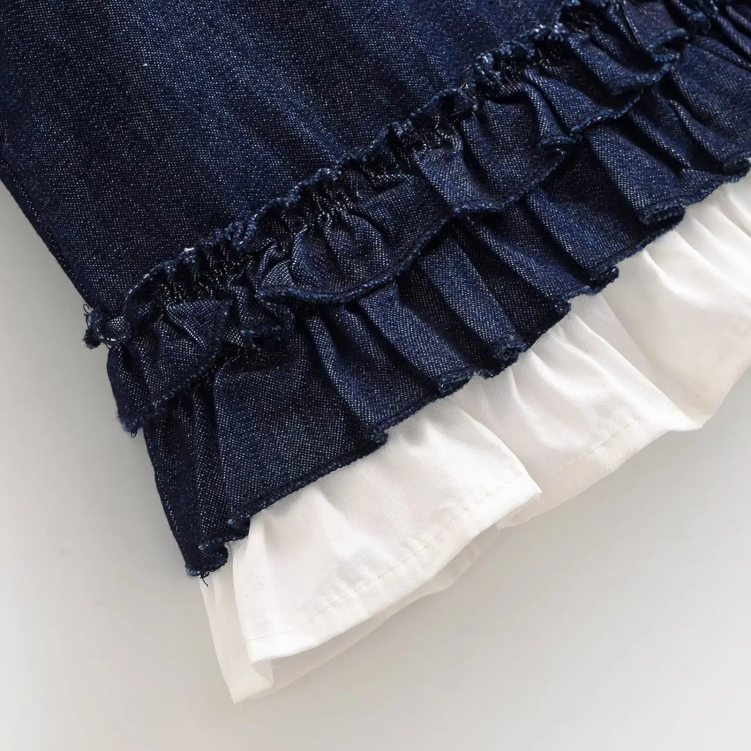 Macro detail shot of double ruffle hem construction, dark denim ruffle stacked over white cotton frill hem stitching