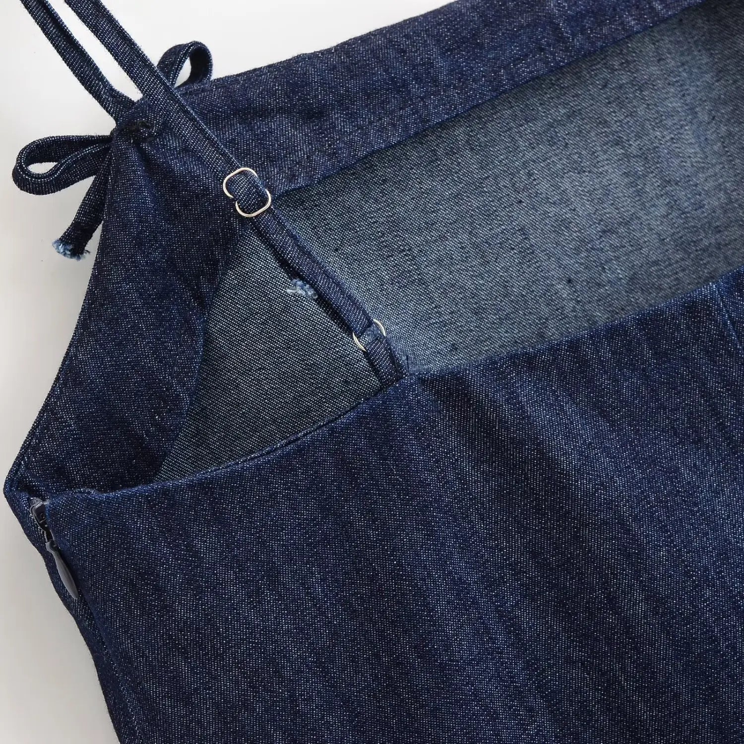 Extreme close‑up of back adjustable slider buckle hardware on denim cami dress, fabric bow tie on shoulder strap, denim woven texture