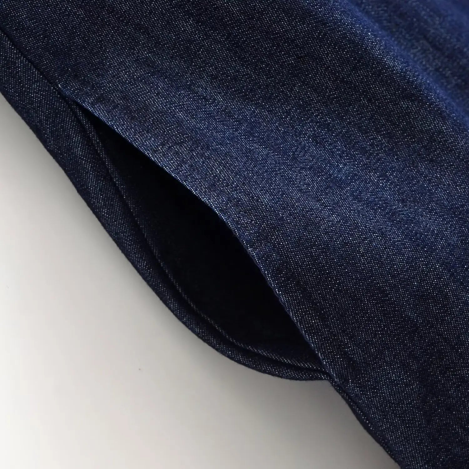 Close‑up view of side invisible zipper seam on dark denim mini dress, woven denim fabric texture detail