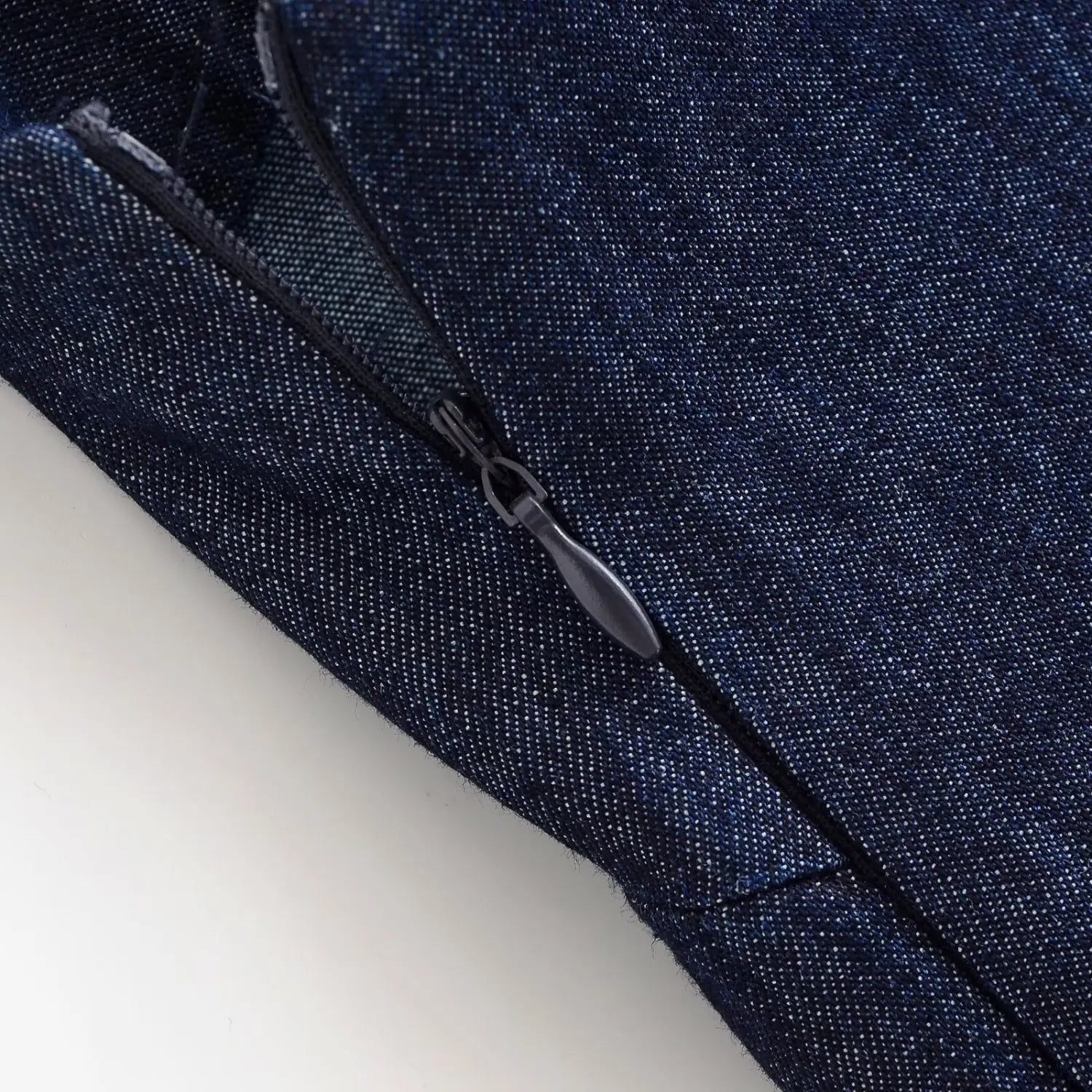 Macro close‑up of side invisible zipper pull on dark denim dress, fine woven denim fabric grain detail