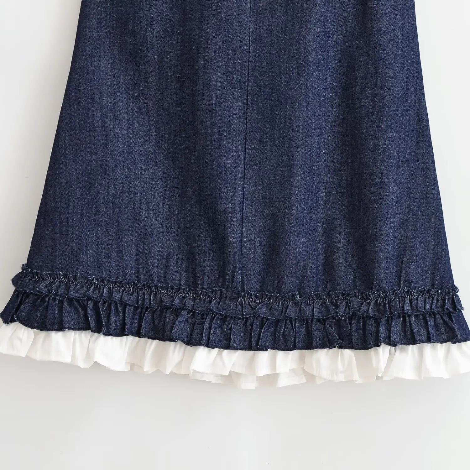 Partial shot of dark denim mini dress skirt hem, double‑layer ruffle design with denim frill overlay white cotton ruffle underlayer, woven denim texture