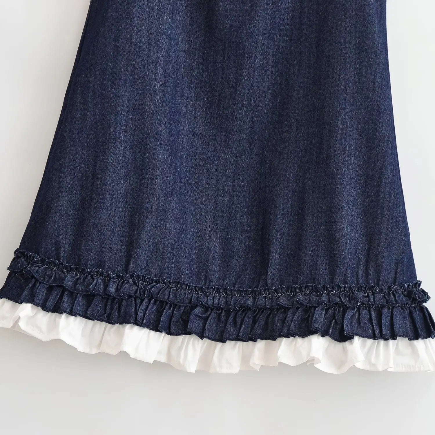 Partial close‑up of dress skirt hem, double‑layer ruffle trim, dark denim outer ruffle and white cotton frill underlayer texture