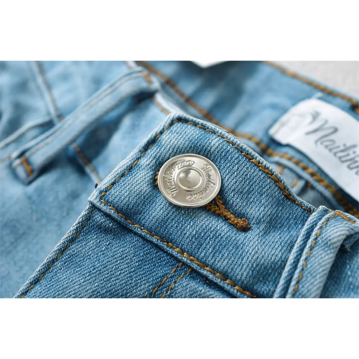 Close-up of the branded metal button on light blue low-rise denim shorts.