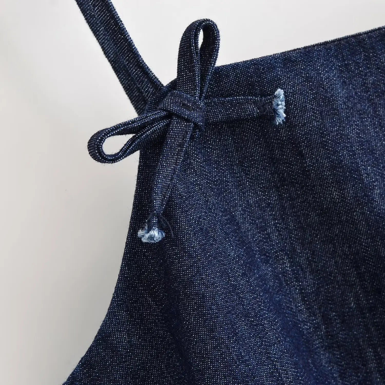 Extreme close‑up of denim fabric shoulder bow tie detail, raw frayed edge tips on spaghetti strap bow