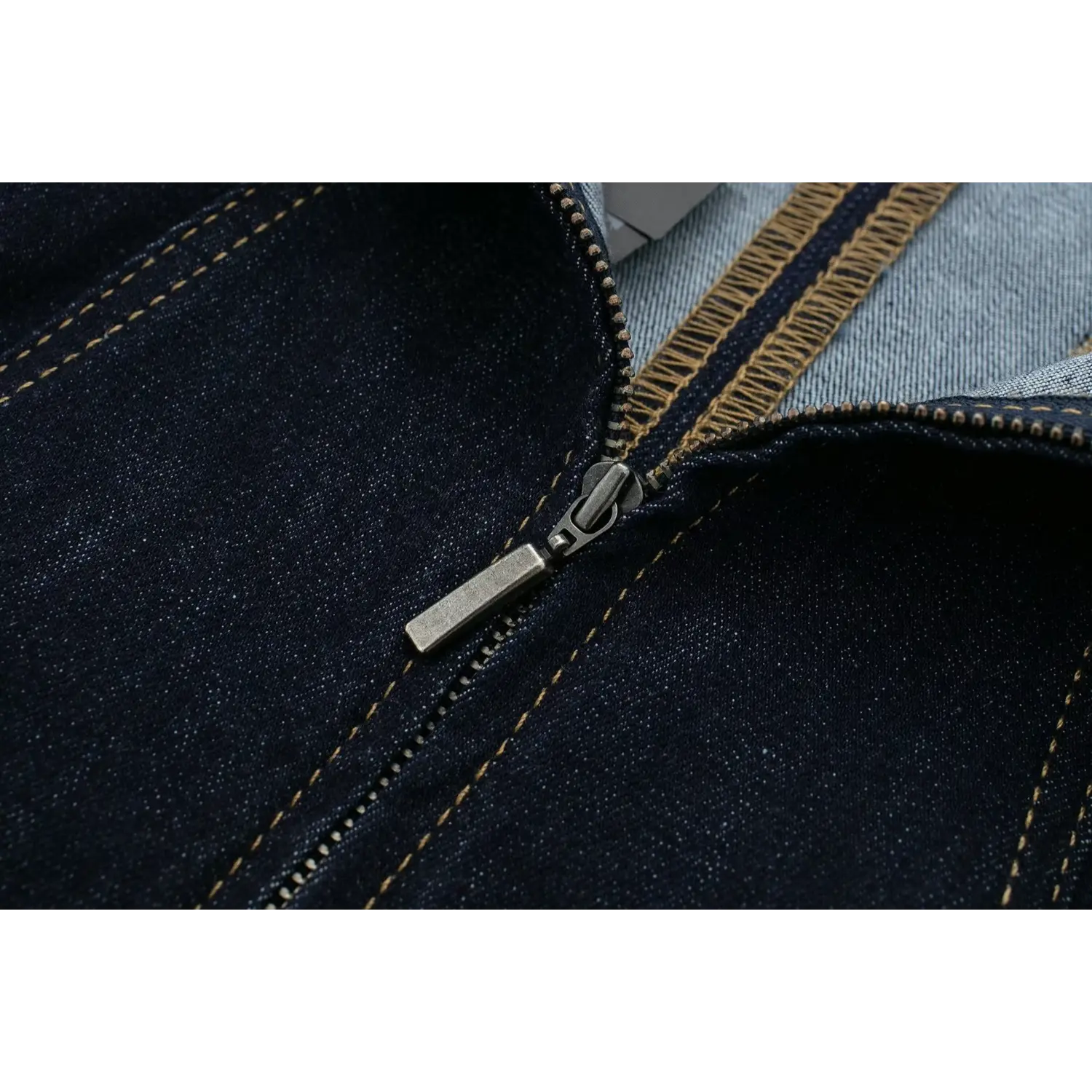 Macro close‑up of antique‑finish metal zipper pull tab and teeth on dark denim strapless dress