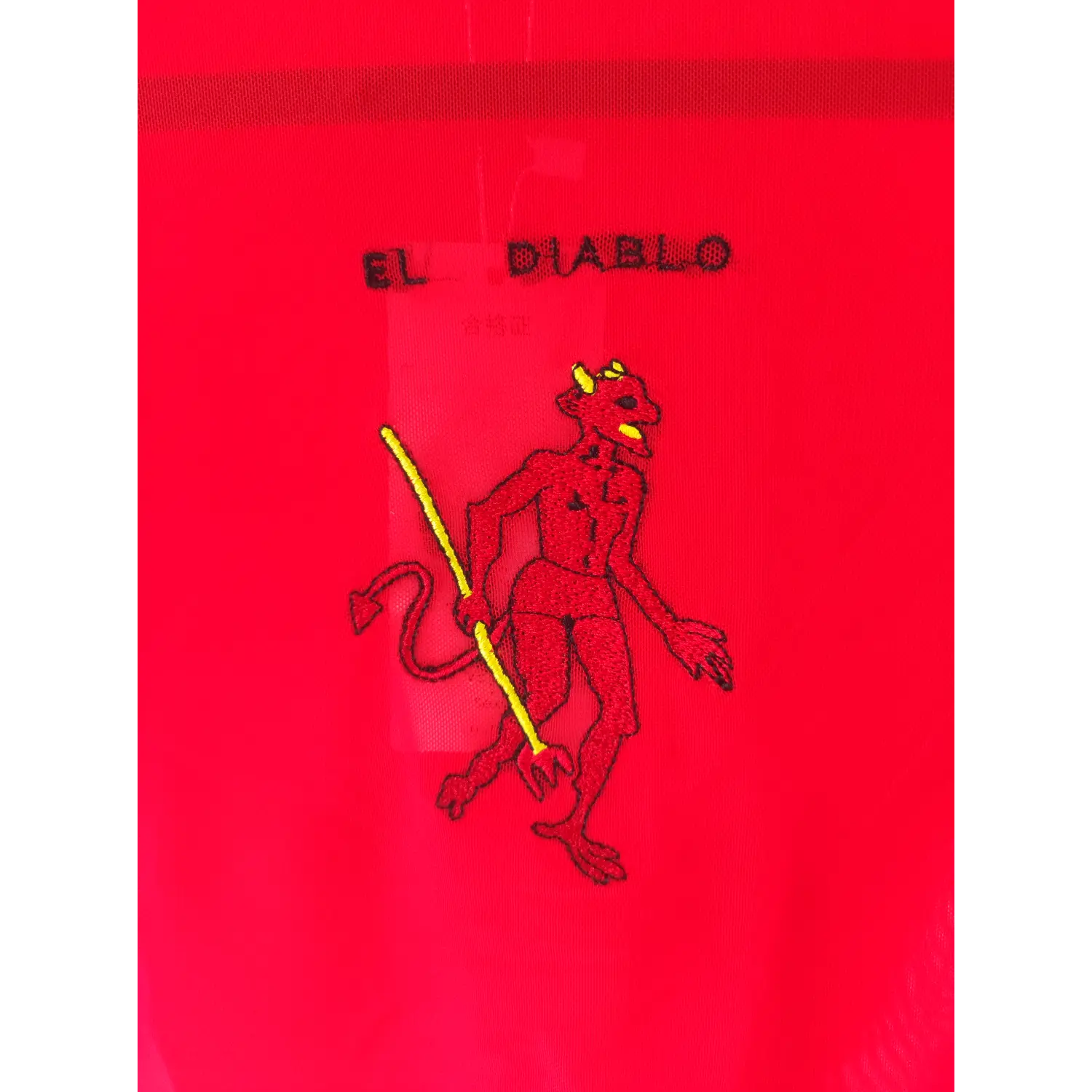 Macro close-up, lettering and devil character embroidery on red mesh top