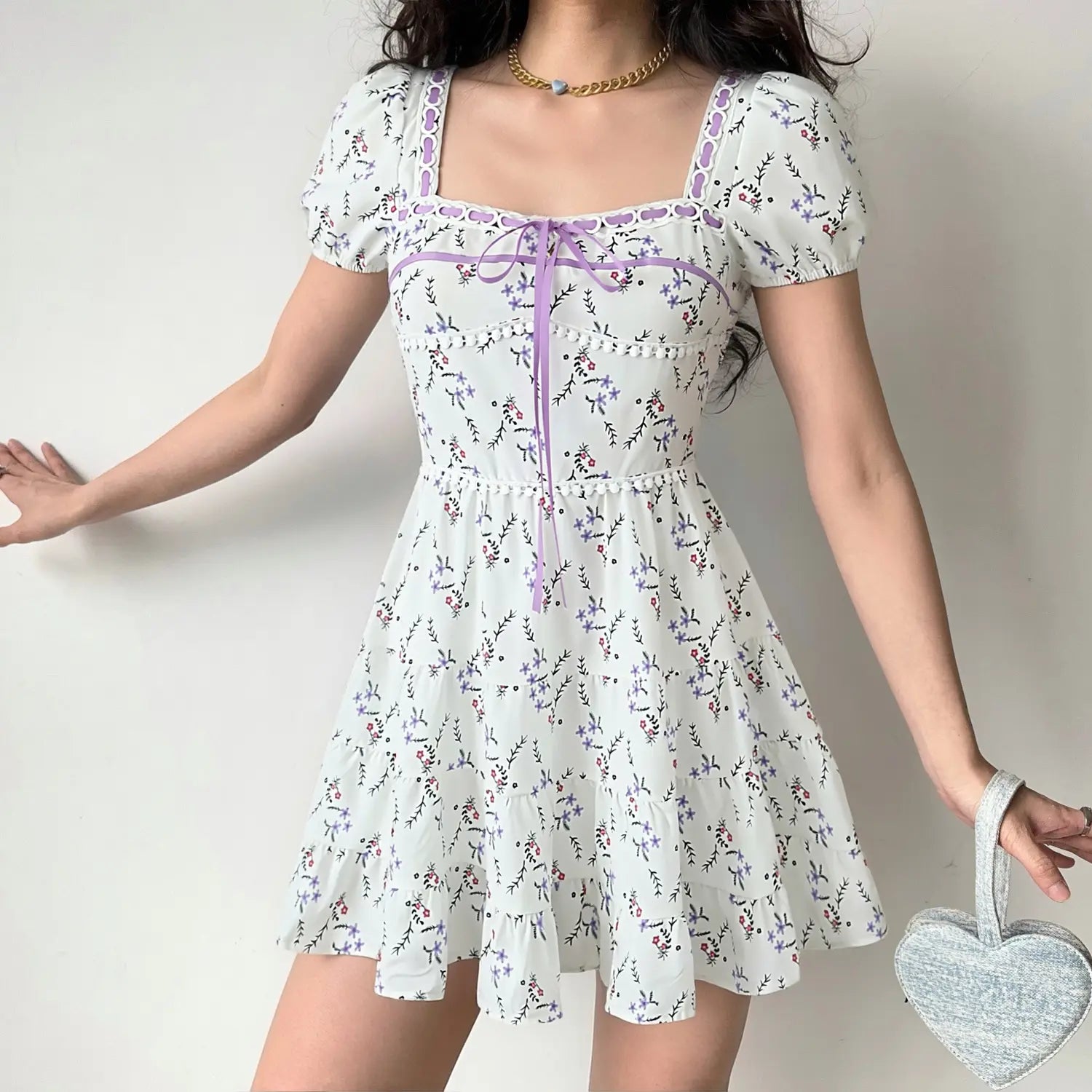 Female model wearing white ditsy floral mini dress, square neck puff sleeve, purple ribbon detail, casual coquette styling